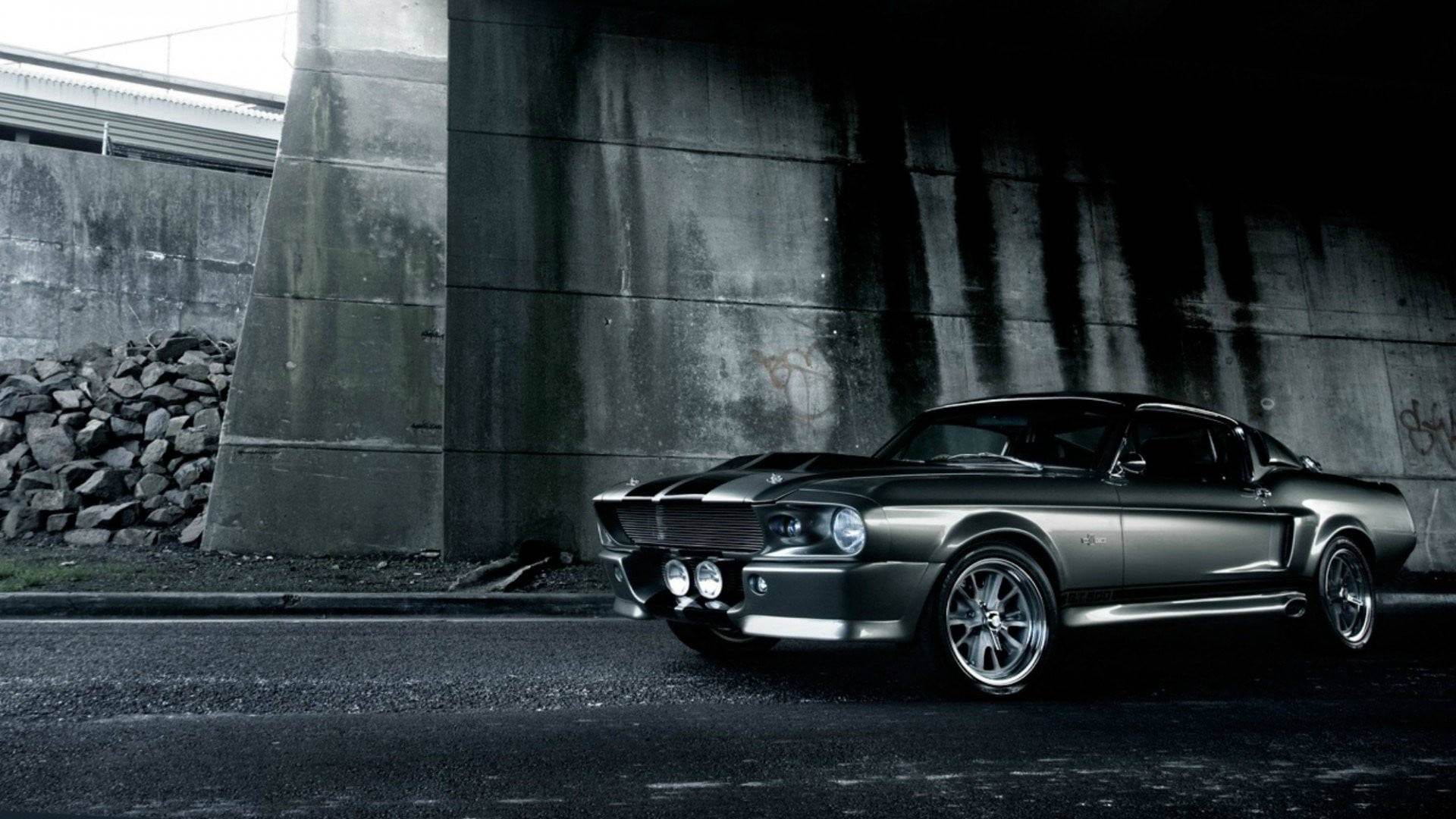 Ford Mustang 桌布 壁紙 — 一架時尚的銀色經典肌肉車停在粗糙的混凝土天橋下，附近有塗鴉和岩石。