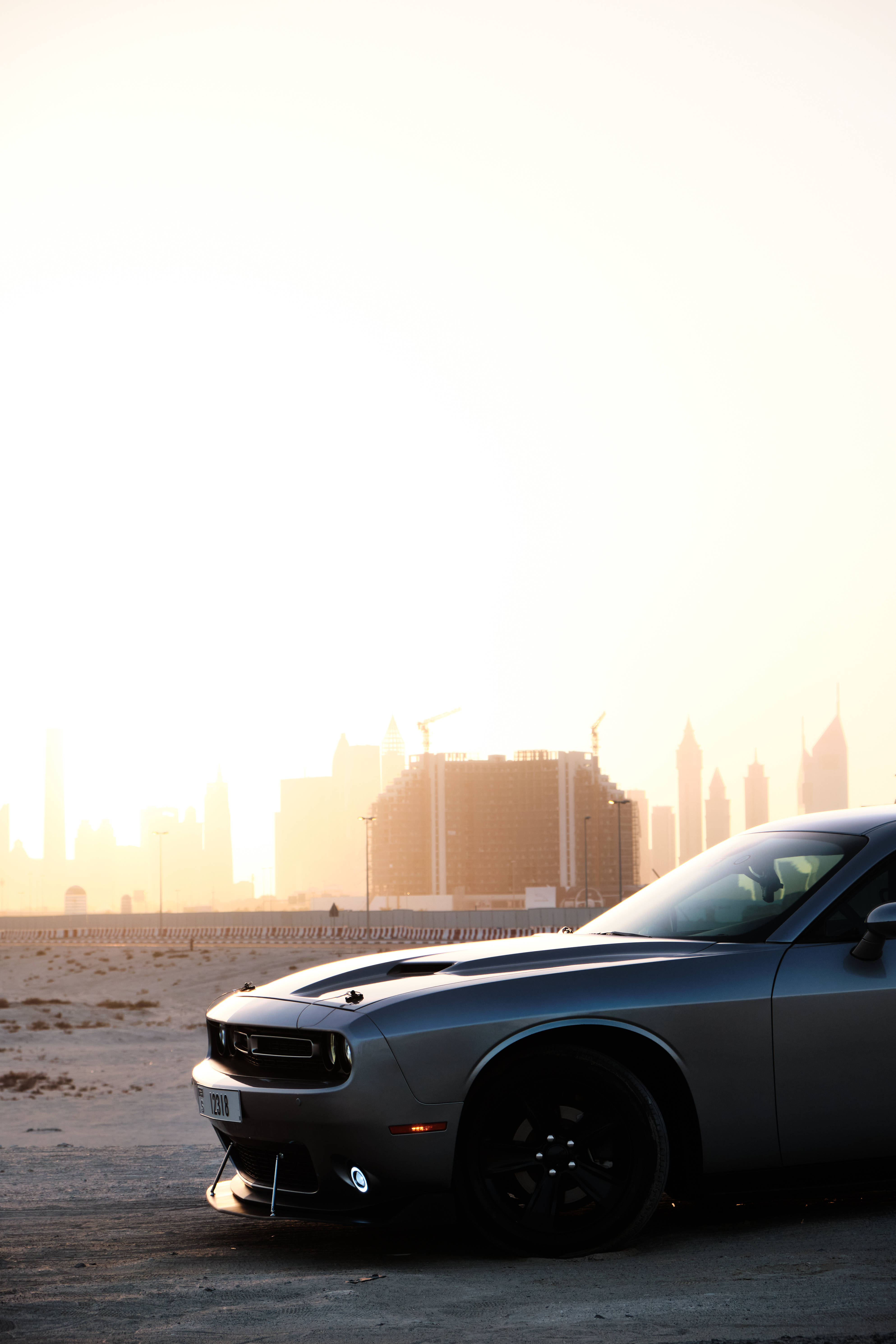 Challenger 桌布 壁紙 — 一架時尚的銀色肌肉車停在沙漠公路上，金色夕陽中隱約可見城市天際線閃耀。