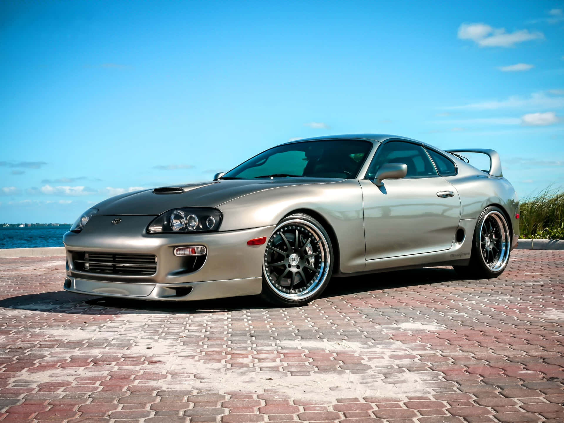 日落時分，銀色豐田Supra跑車停泊在靠近海洋的磚砌碼頭上。 — Toyota Supra Mk4 壁紙
