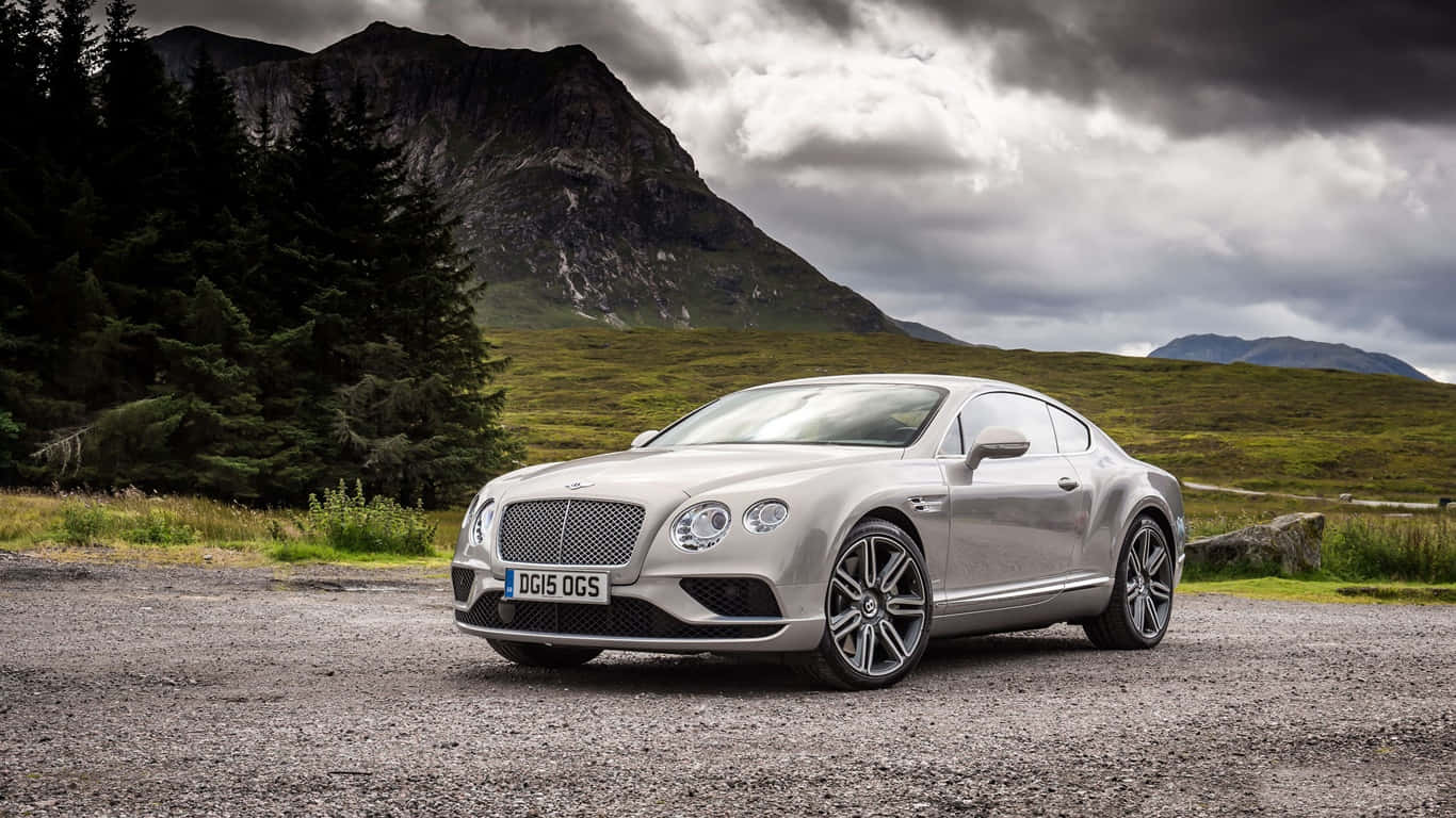 1366x768 Bentley 桌布 壁紙 — 一架時尚的銀色賓利 Continental GT 停泊在碎石路上，背景是戲劇性的山脈和烏雲。