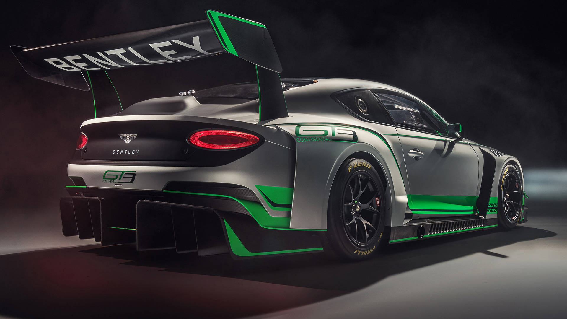 bentley HD 桌布 壁紙 — 一架時尚的銀色賓利 Continental GT3 賽車，帶有充滿活力的綠色飾邊和大型後尾翼，在充滿煙霧和聚光燈的戲劇性工作室環境中展示。