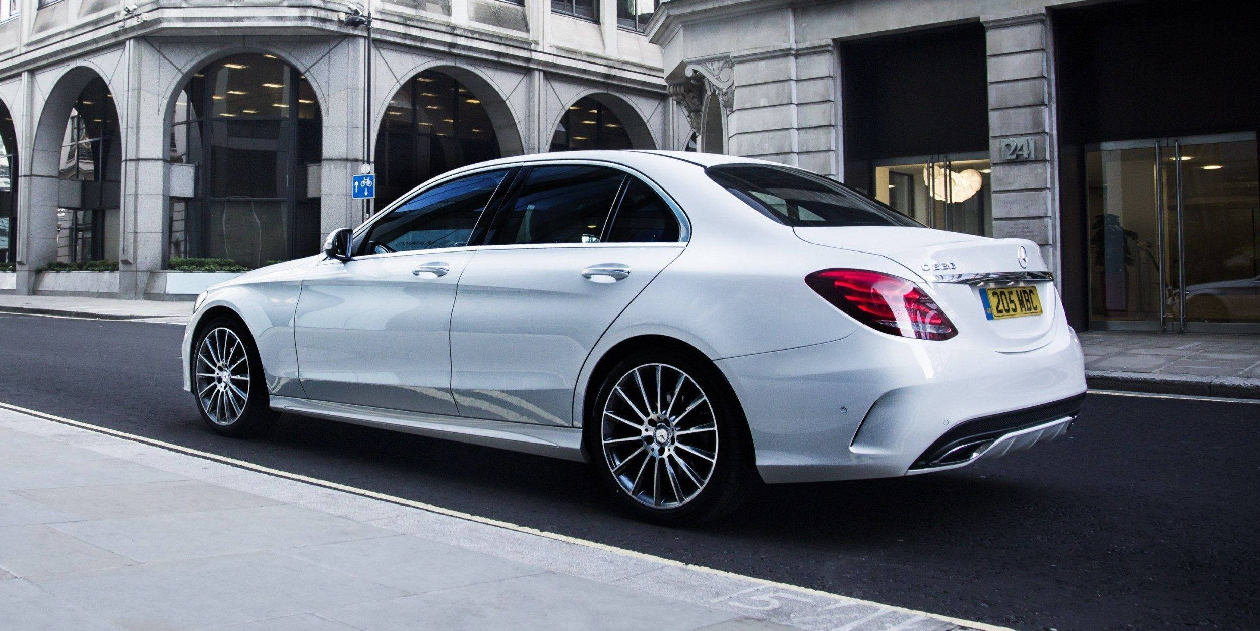 Mercedes Benz C300 桌布 壁紙 — 一架時尚的銀色賓士轎車停放在城市街道上，旁邊是拱形窗戶的石建築。