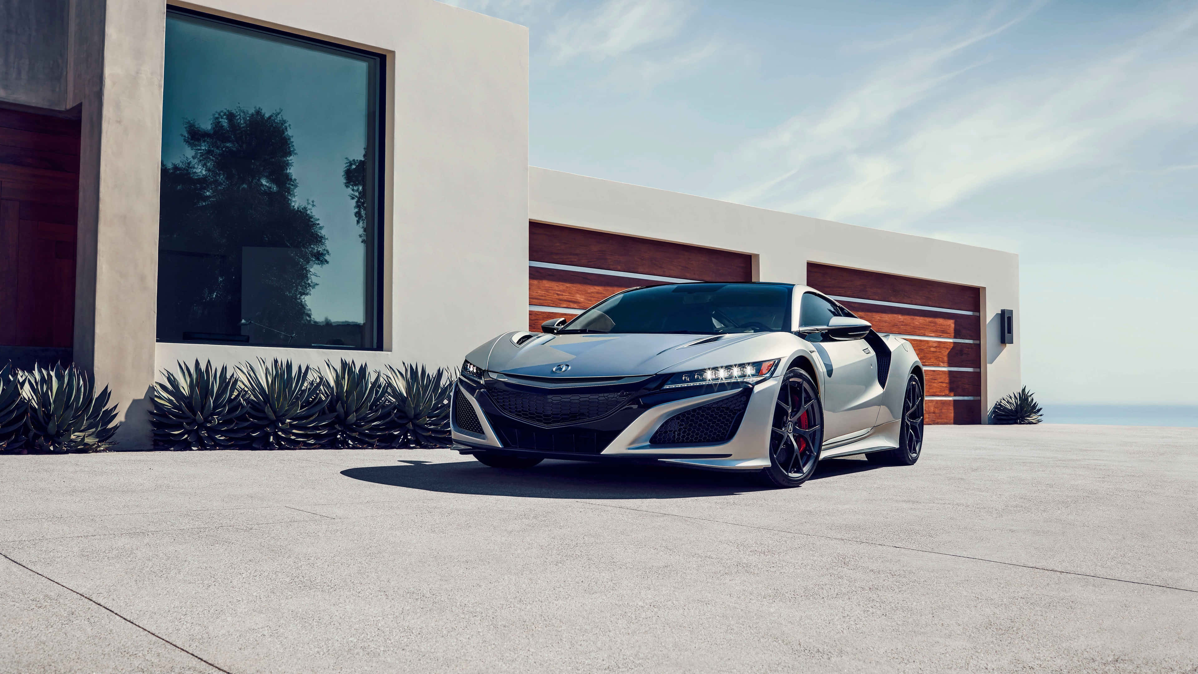 Acura Nsx 桌布 壁紙 — 一架時尚的銀色跑車停放在混凝土車道上，前方是一棟現代簡約風格的房子，擁有大型窗戶和木製車庫門。