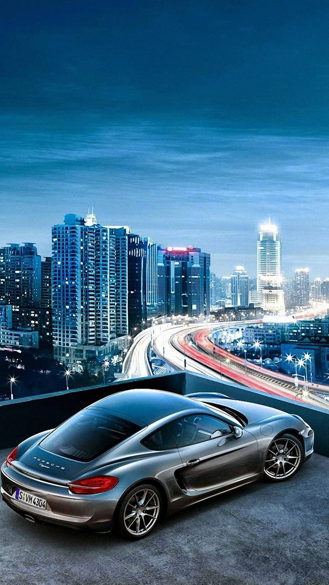 高清汽車 桌布 壁紙 — 一架時尚的銀色跑車停泊在屋頂上，俯瞰著暮色中充滿活力的城市景觀，伴隨著發光的交通軌跡。