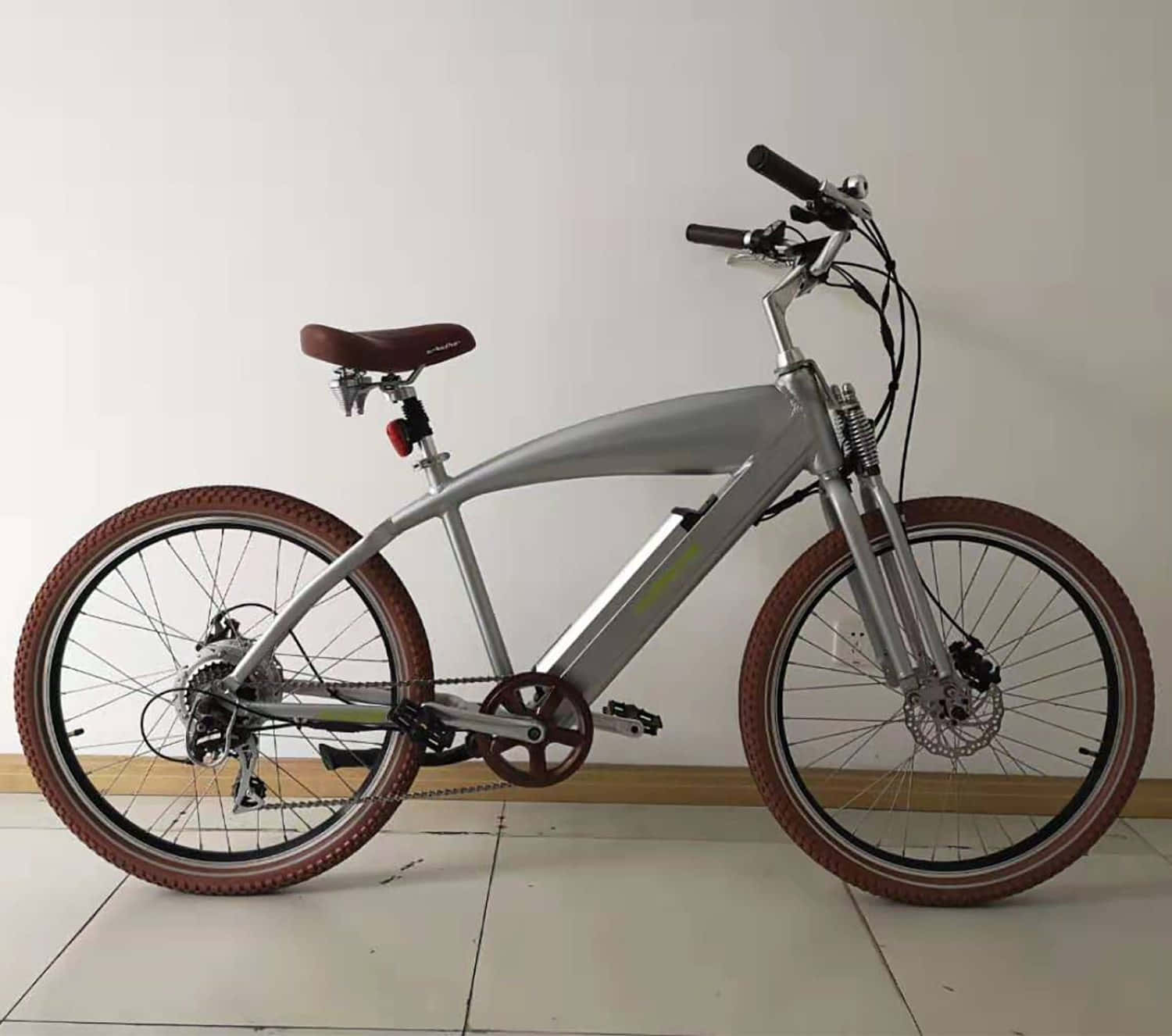 Beach Cruiser 桌布 壁紙 — 一架時尚的銀色電動自行車，配備棕色輪胎和座椅，室內靠著純白牆壁停放。