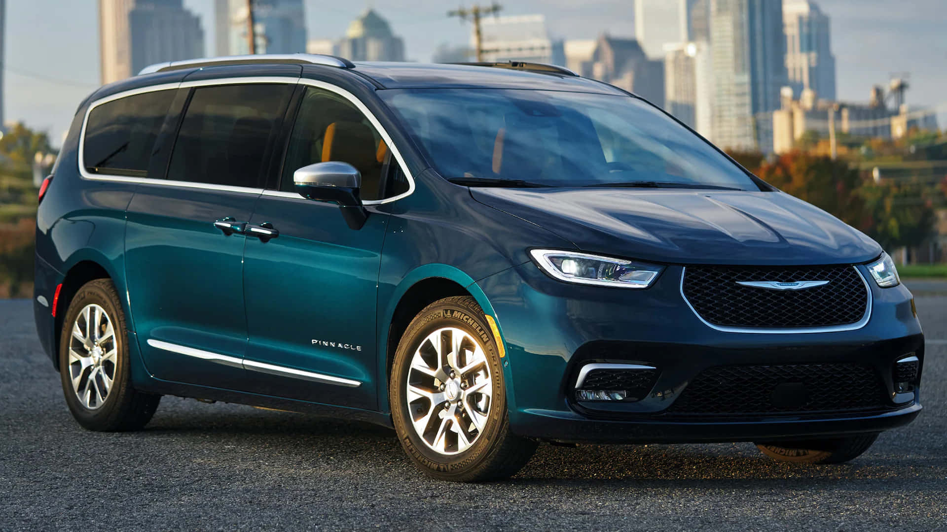 Chrysler Pacifica 桌布 壁紙 — 一架時尚的青綠色 Chrysler Pacifica 小型貨車停泊在瀝青路上，背景是現代城市天際線。