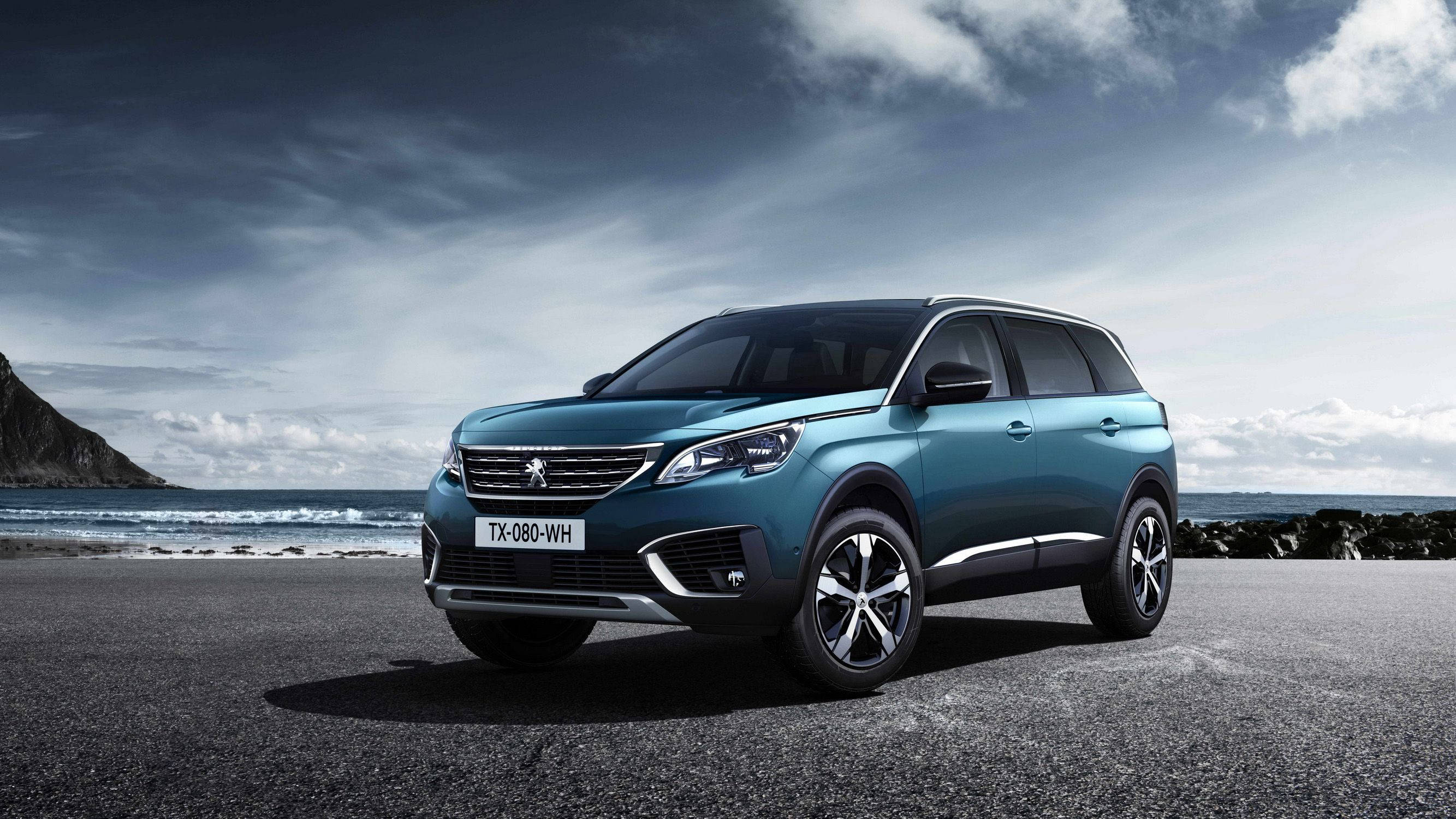 Peugeot 桌布 壁紙 — 一架時尚的青綠色SUV停泊在沿海公路上，背景是戲劇性的雲層和海洋波浪。