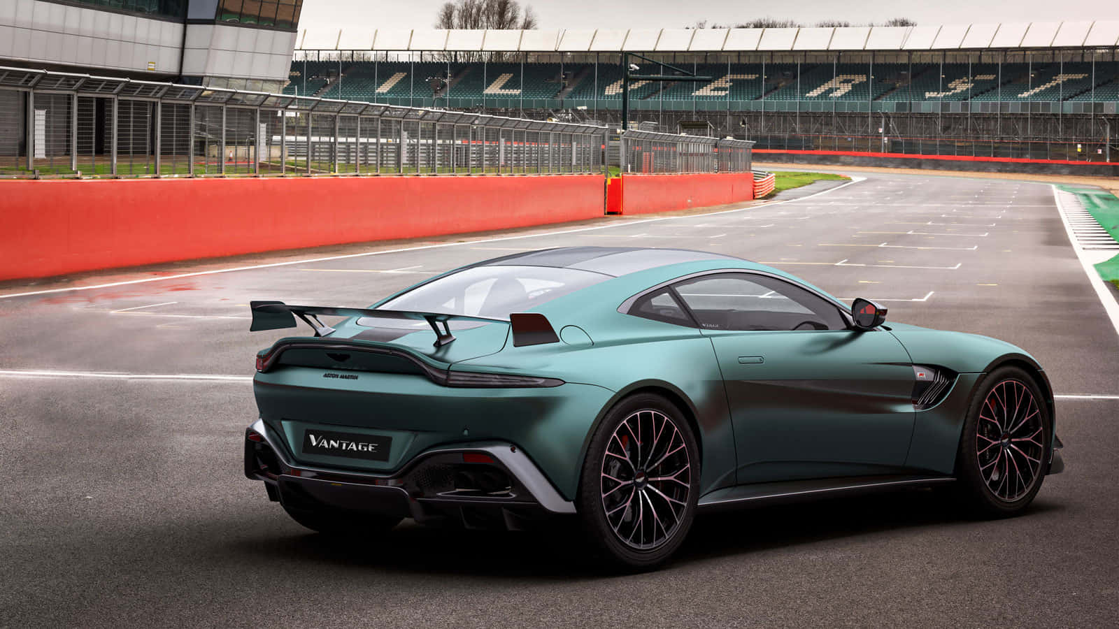 奧斯頓馬丁 桌布 壁紙 — 一架時尚的青色 Aston Martin Vantage 跑車停在濕滑的賽道上，背景有看台。