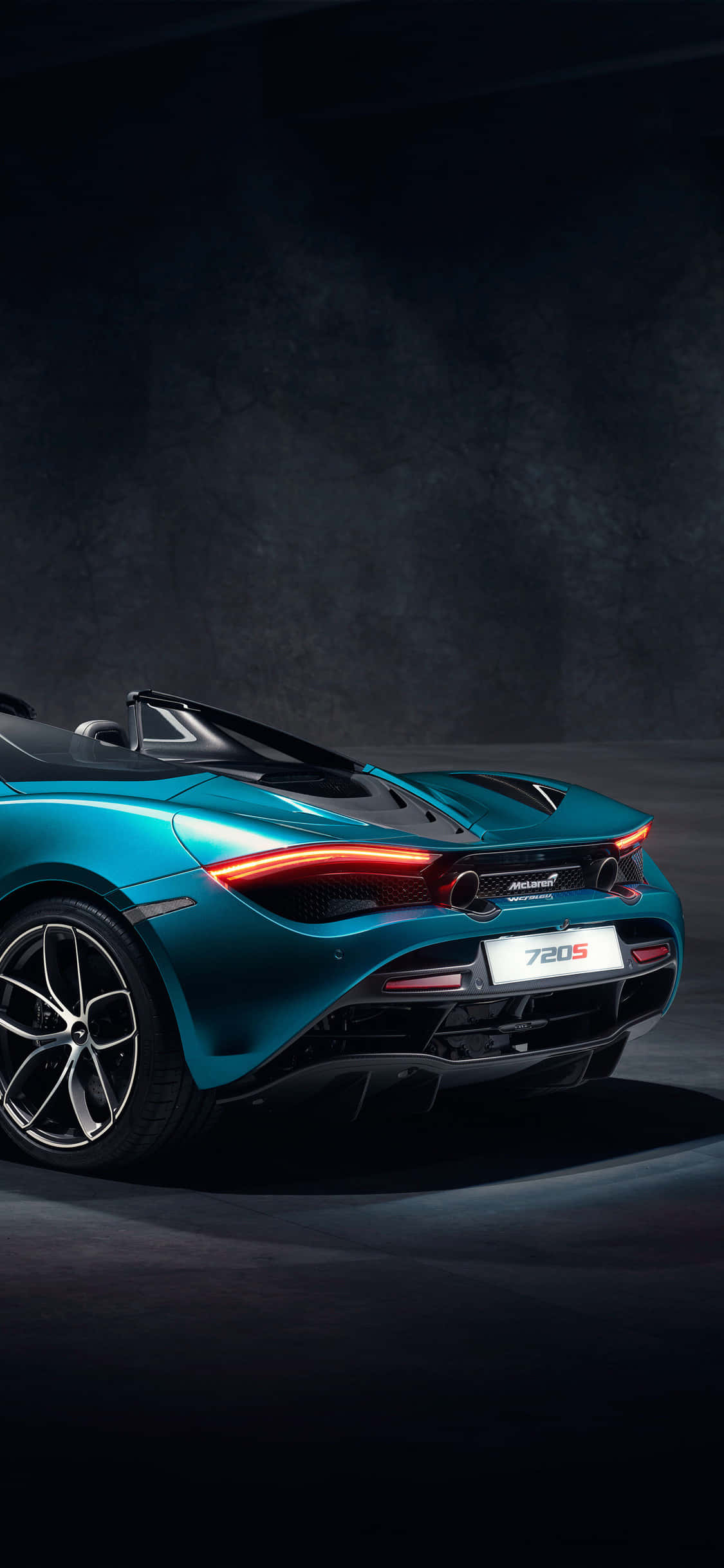Blue Car 桌布 壁紙 — 一架時尚的青色McLaren 720S Spider敞篷車在戲劇性的攝影棚燈光下，在深色紋理牆壁前閃閃發光。