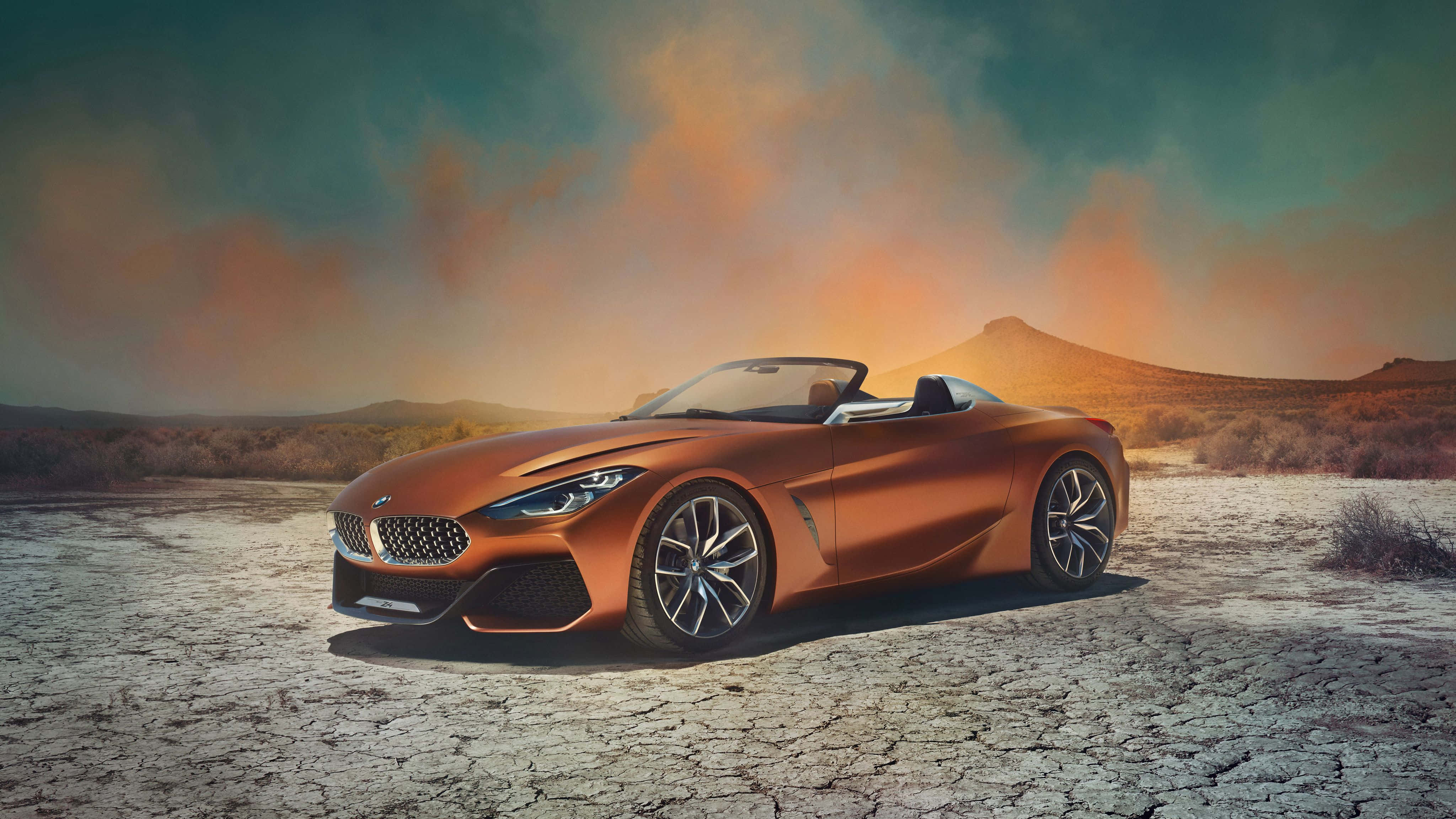 Bmw Z4 桌布 壁紙 — 一架時尚的青銅色敞篷跑車停放在龜裂的沙漠地上，背景是戲劇性的日落天空。