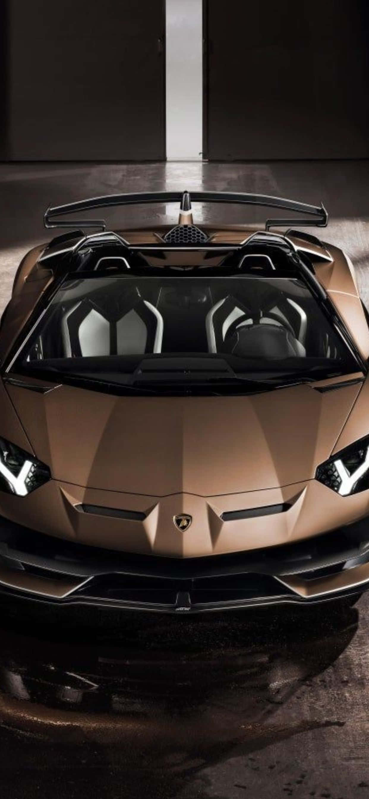 Lamborghini Phone 桌布 壁紙 — 一架時尚的青銅色藍寶堅尼跑車，黑色車頂，停在昏暗的車庫中，其侵略性設計和發光的車頭燈引人注目。