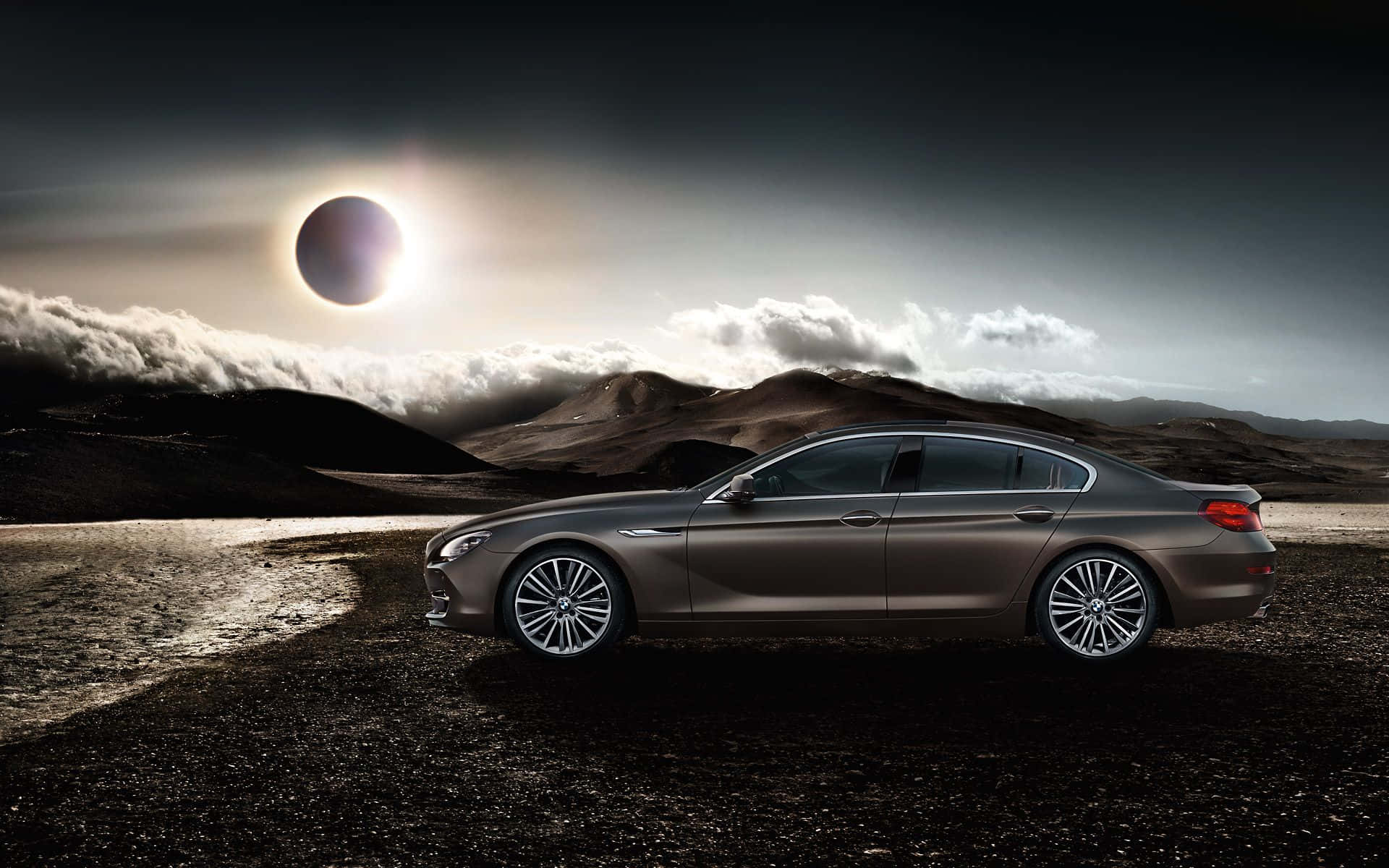 Bmw 6 Series 桌布 壁紙 — 一架時尚的青銅色轎車停泊在火山景觀上，背景是帶有雲層的戲劇性日食。