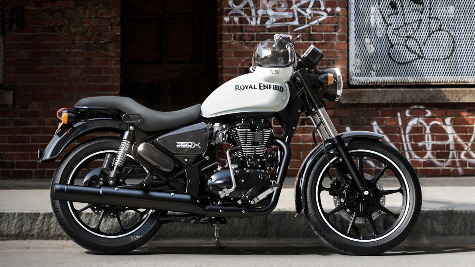  壁紙 — 一架時尚的黑白Royal Enfield 350X摩托車停放在人行道上，旁邊是佈滿塗鴉的磚牆。