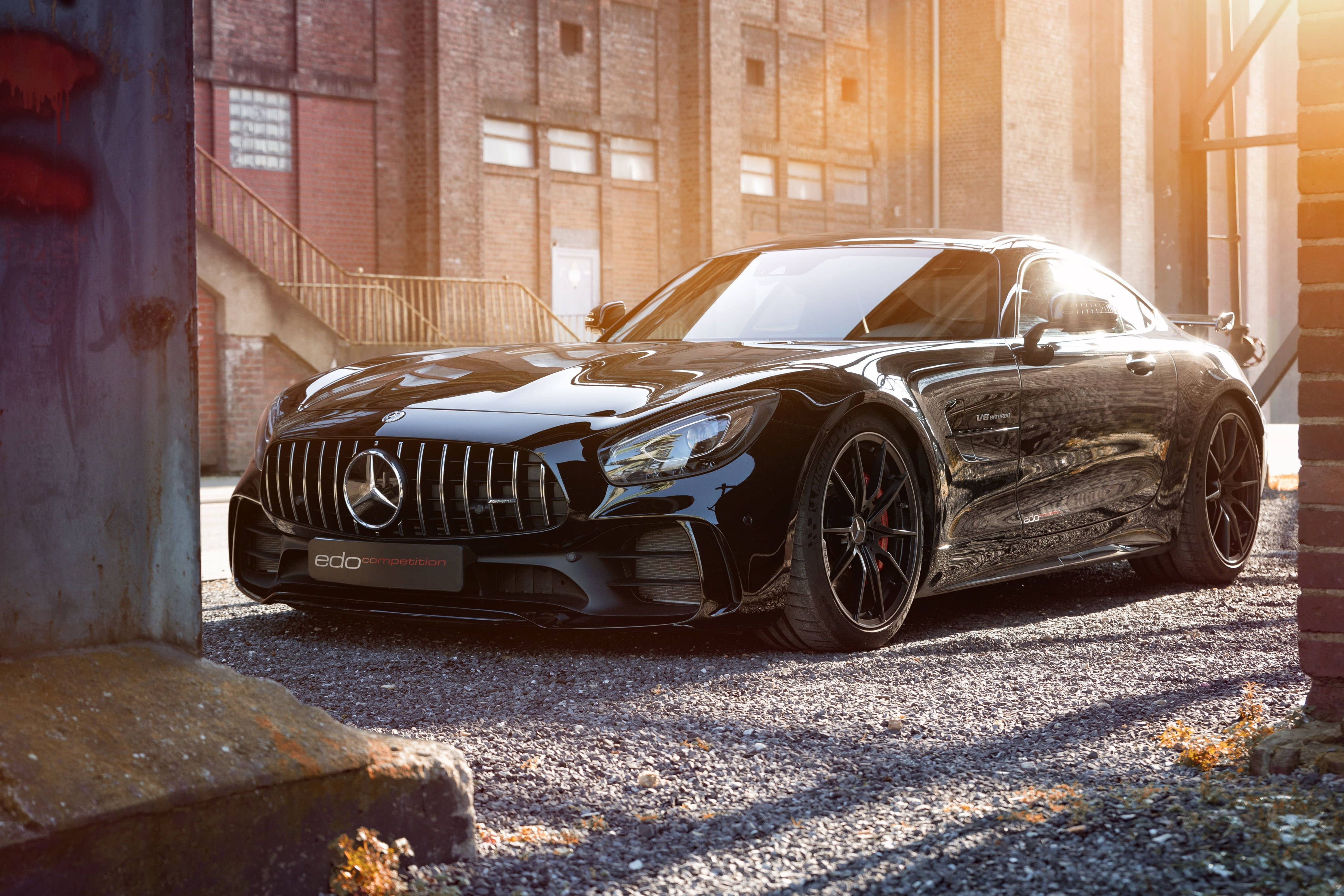 Mercedes 桌布 壁紙 — 一架時尚的黑色 Mercedes-AMG GT 停放在工業小巷中，陽光在其光澤表面閃爍。