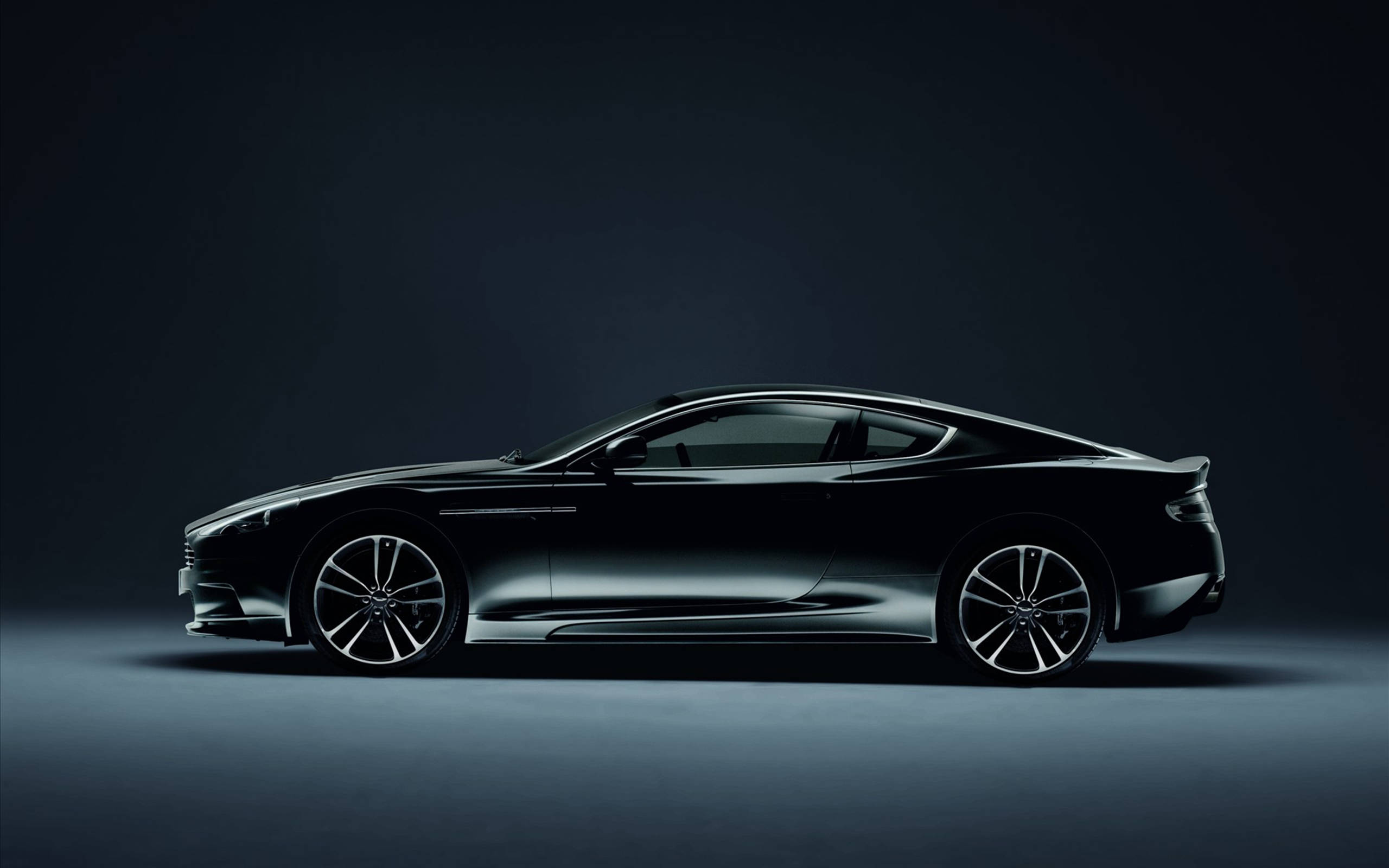 cars 桌布 壁紙 — 一架時尚的黑色Aston Martin跑車在昏暗的攝影棚背景下，以側面輪廓滑行，配以戲劇性的燈光。