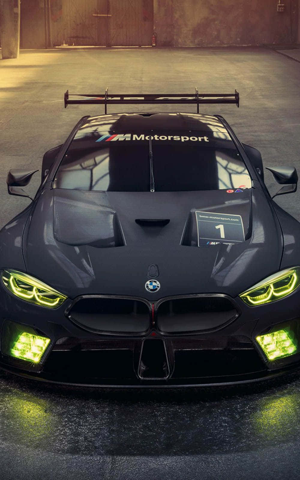 BMW 動圖 桌布 壁紙 — 一架時尚的黑色BMW M Motorsport賽車，帶有發光的綠色頭燈，停放在燈光昏暗的車庫中。