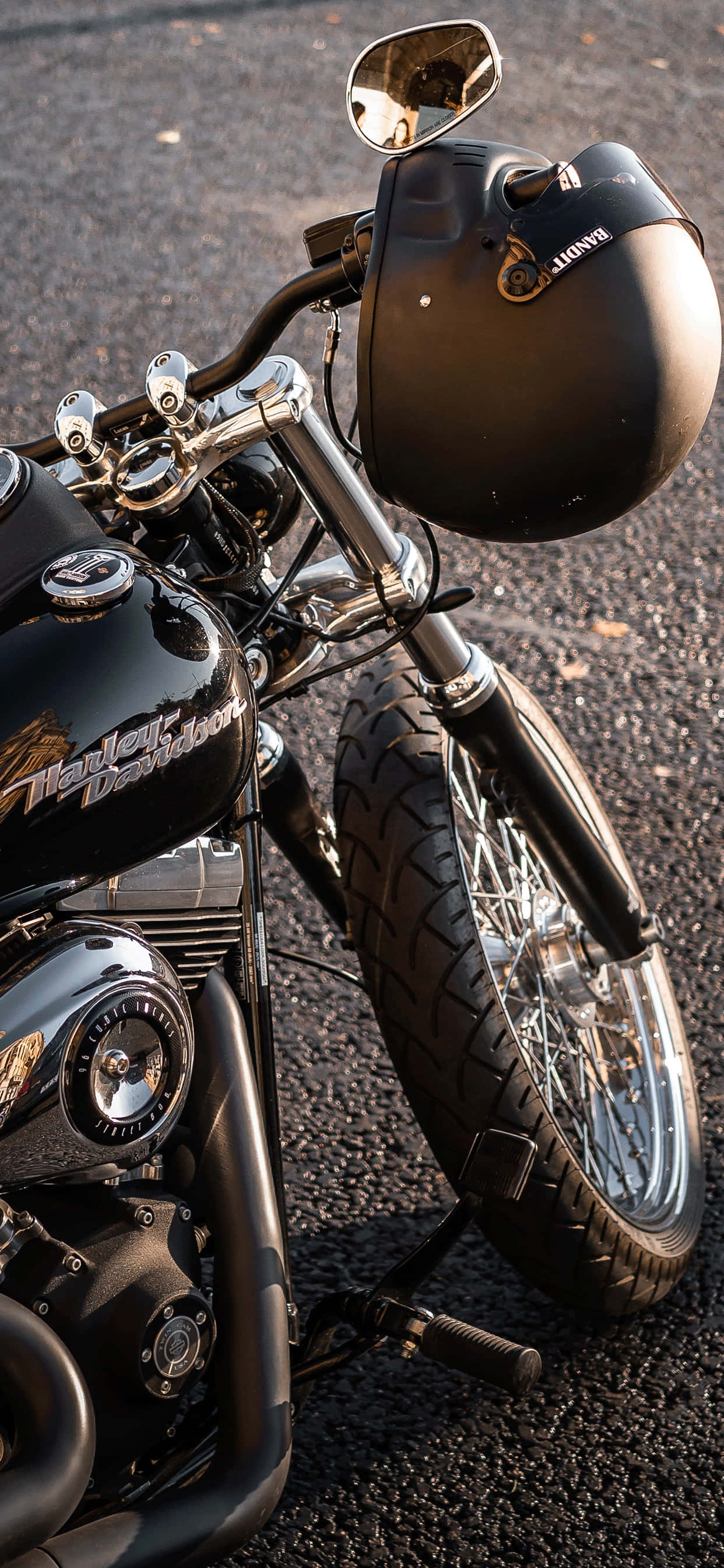 哈雷戴維森 桌布 壁紙 — 一架時尚的黑色Harley-Davidson機車連同安全帽停泊在柏油路上，沐浴在溫暖的金色光芒中。