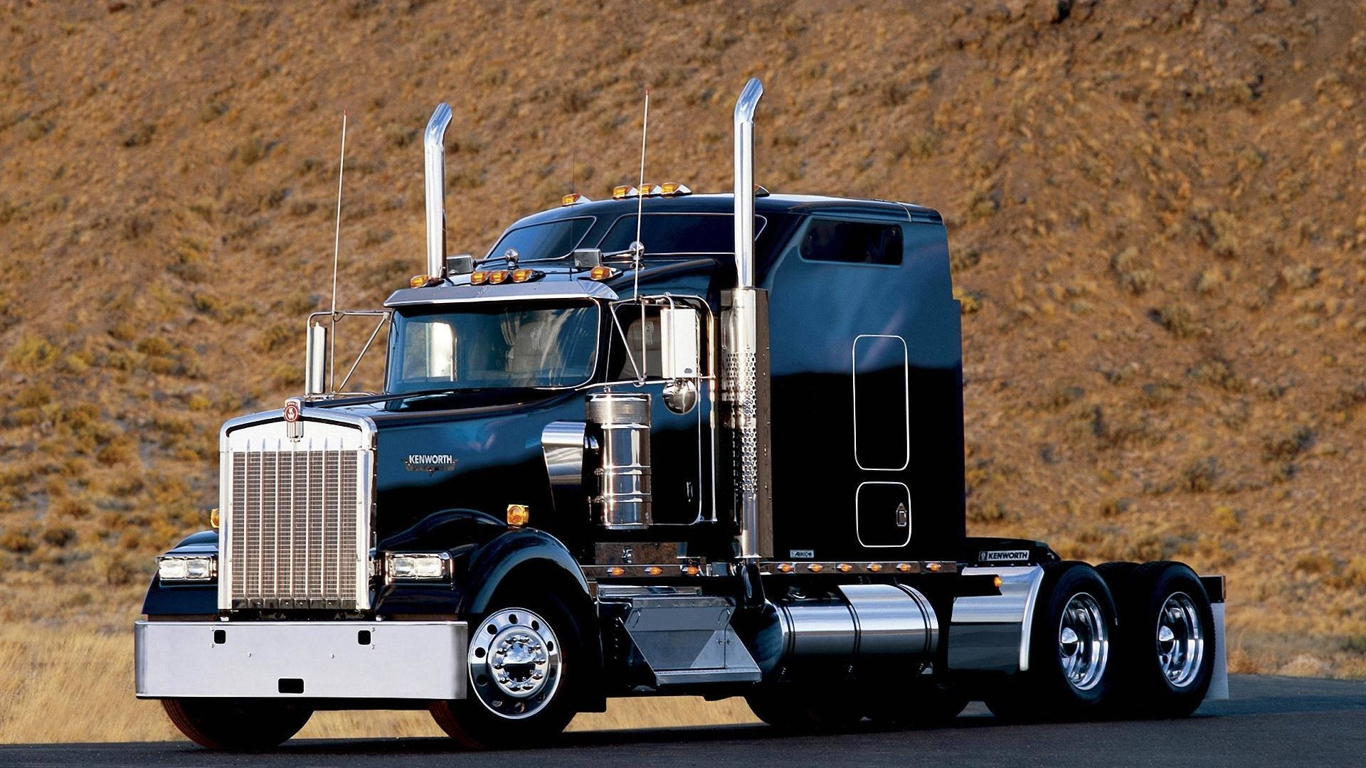 Kenworth 桌布 壁紙 — 一架時尚的黑色Kenworth半掛卡車帶有鍍鉻裝飾，停在沙漠公路上，背景是崎嶇的棕色山丘。