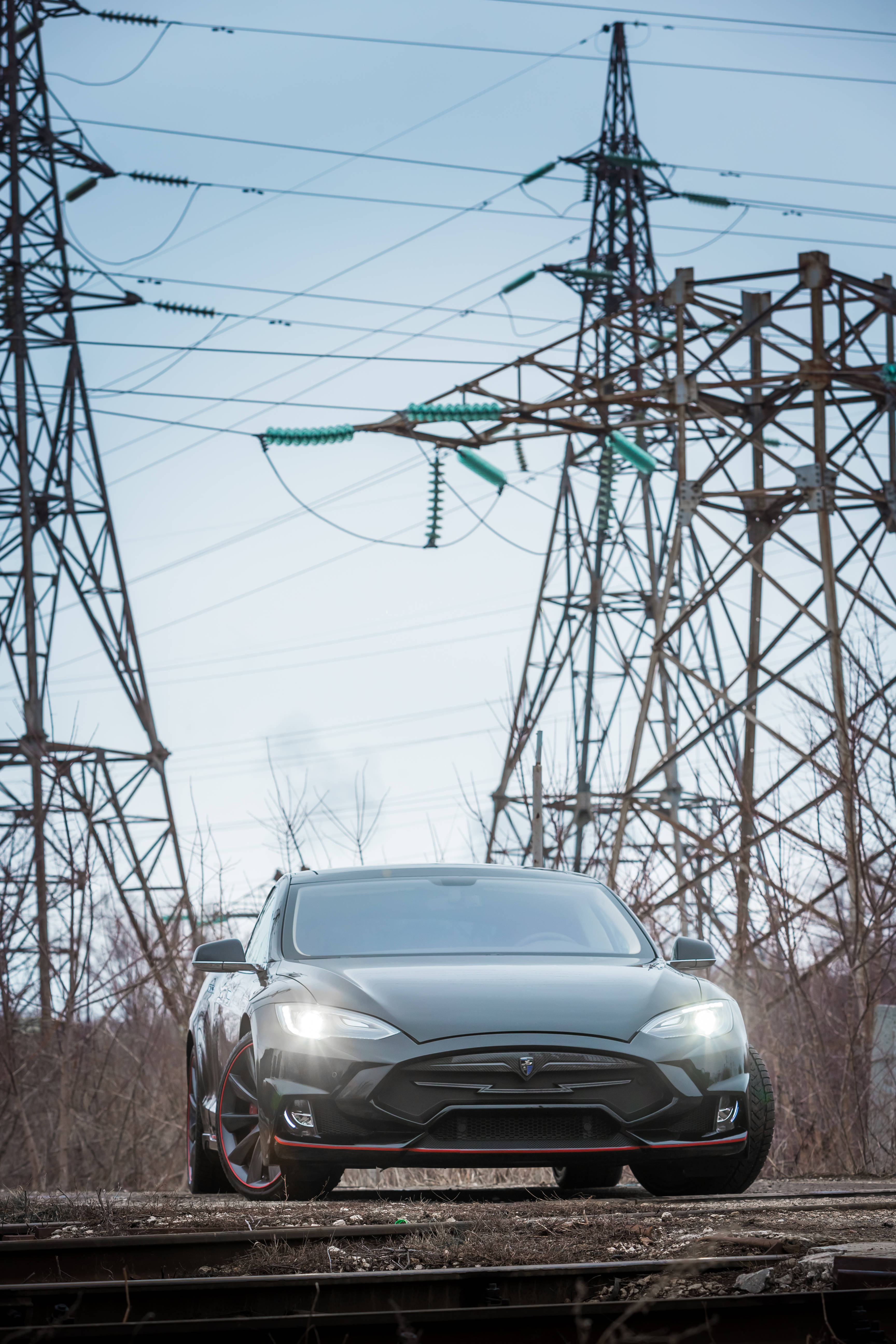 特斯拉 桌布 壁紙 — 一架時尚的黑色Tesla Model S停在生鏽的火車軌道上，上方是高聳的電線，背景是蒼白的天空。