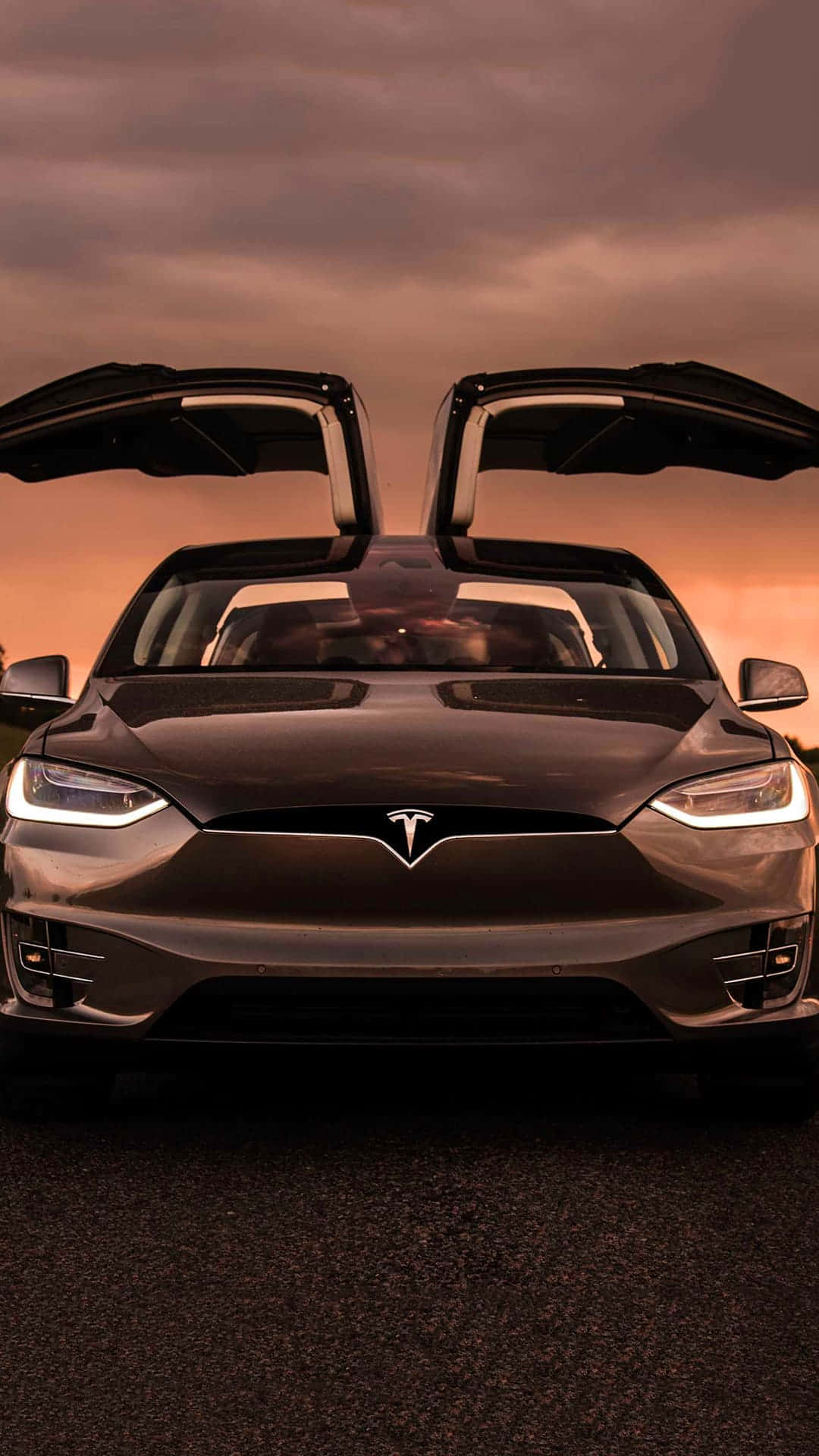 特斯拉 桌布 壁紙 — 一架時尚的黑色Tesla，打開鷗翼車門，在戲劇性的日落天空下蓄勢待發。