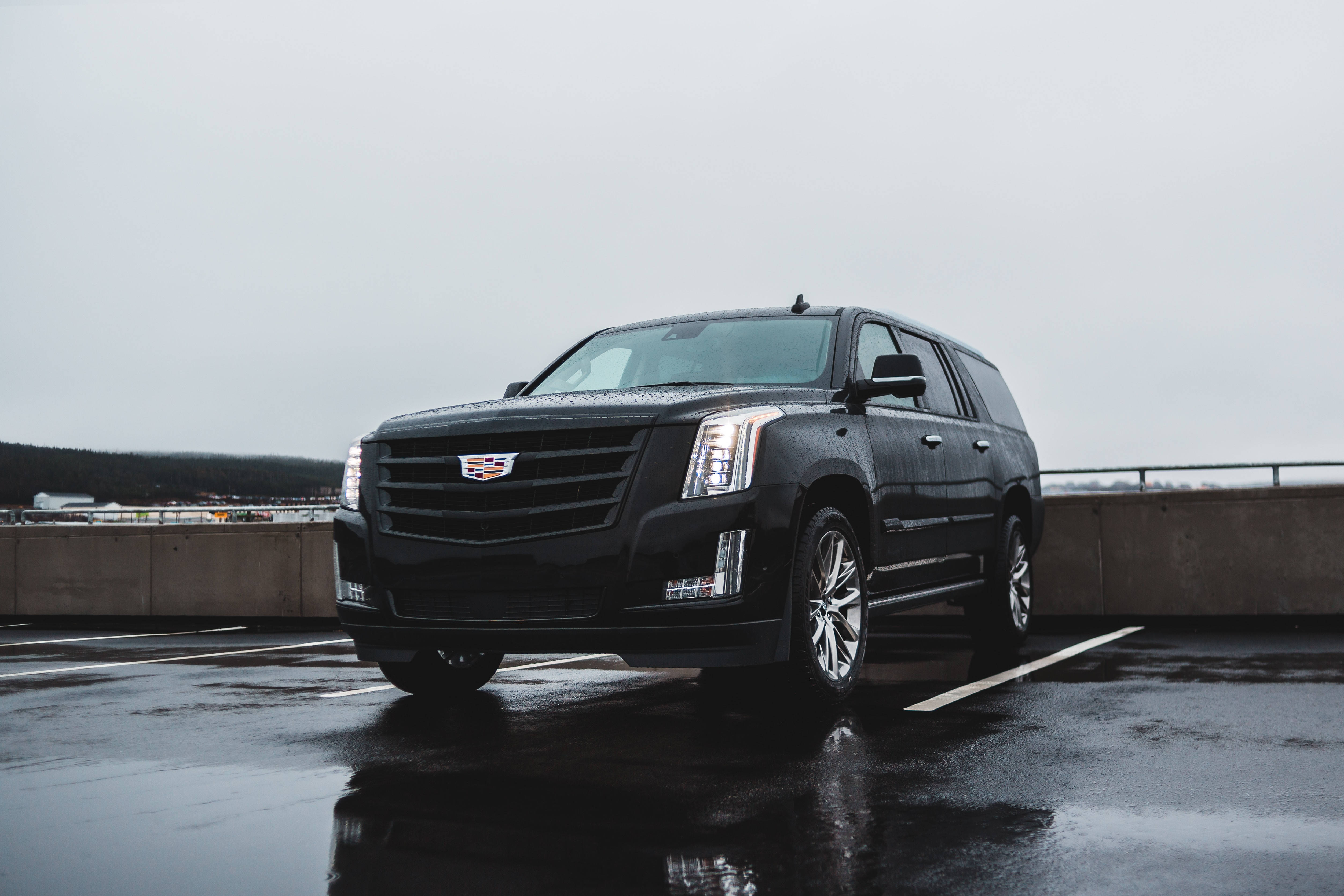 Cadillac 桌布 壁紙 — 一架時尚的黑色凱迪拉克 Escalade 停泊在潮濕的屋頂停車場，天空多雲。