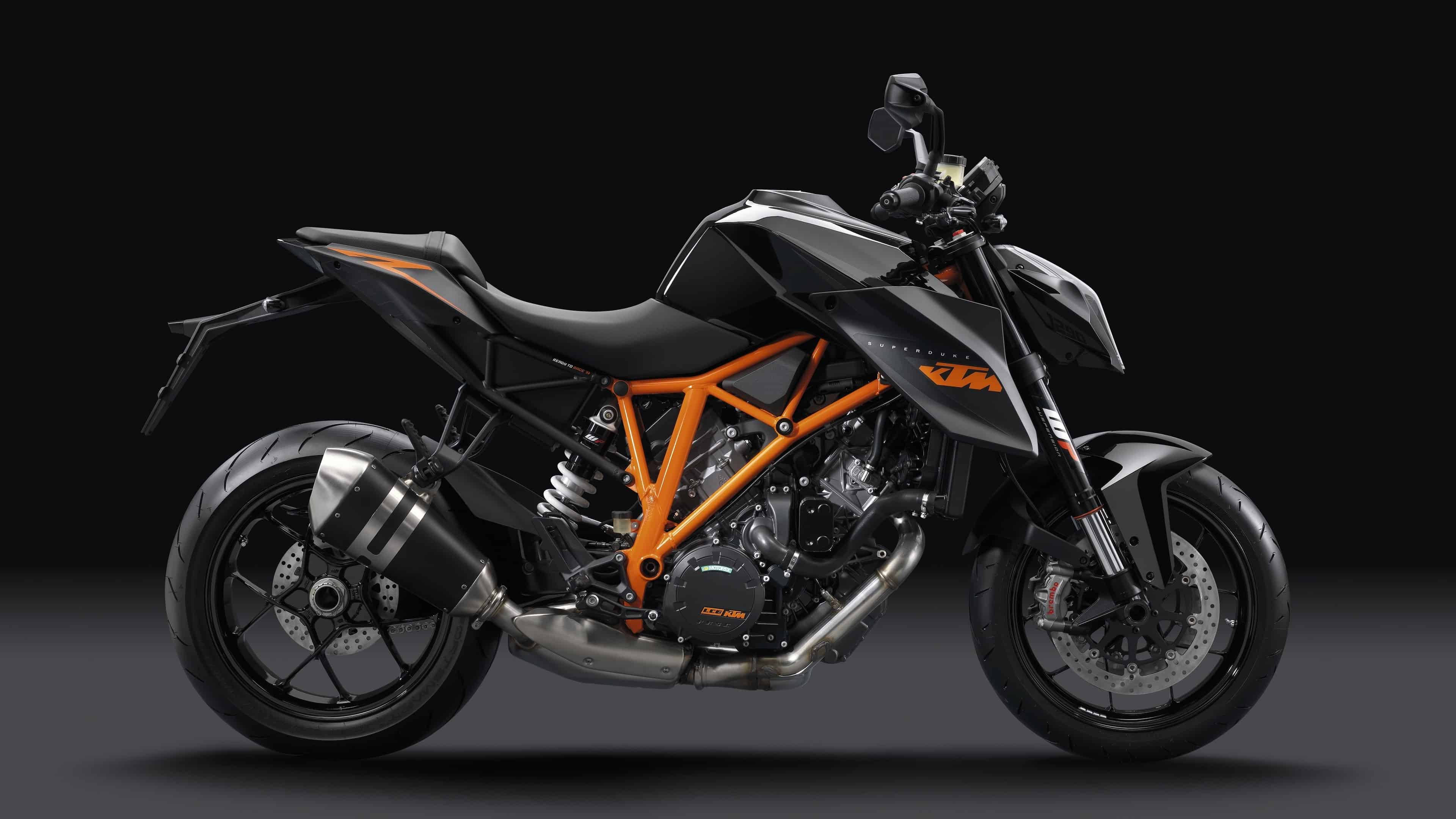 KTM RC 200 桌布 壁紙 — 一架時尚的黑色和橙色KTM摩托車，帶有外露引擎和鍍鉻排氣管，在黑暗的攝影棚中配合戲劇性燈光。