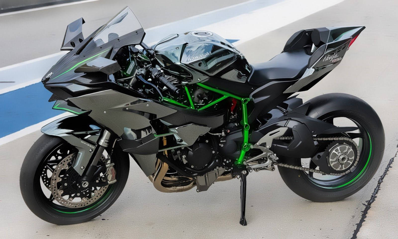 機車 桌布 壁紙 — 一架時尚的黑色和綠色 Kawasaki Ninja 運動機車，帶有外露車架，站立在賽道表面上。