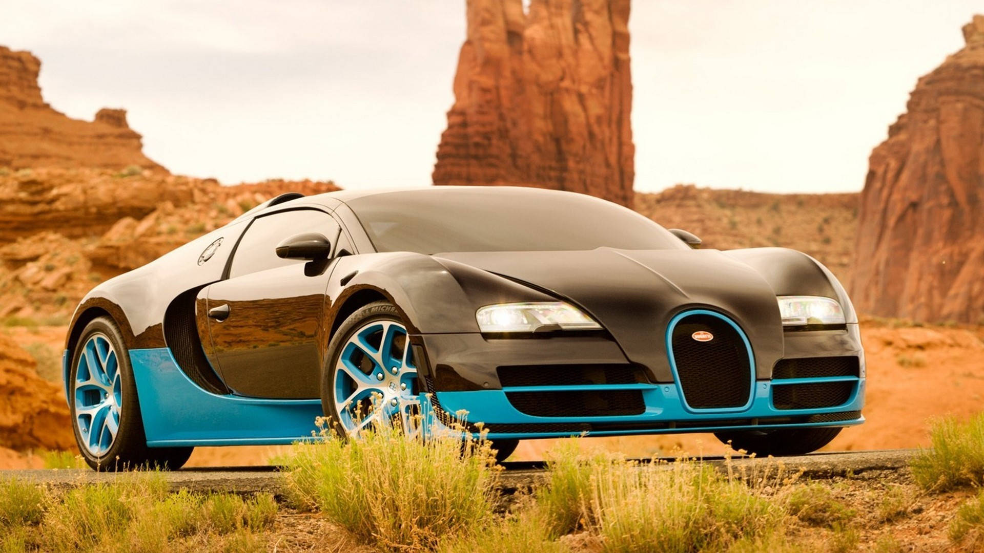 Cool Bugatti 桌布 壁紙 — 一架時尚的黑色和藍色Bugatti Veyron停泊在沙漠公路上，背景是紅色岩層。