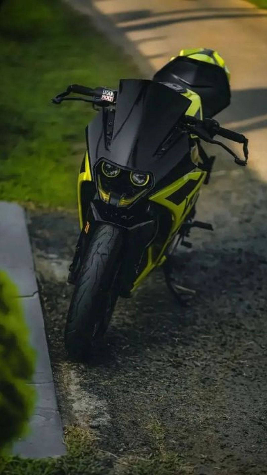 KTM RC 200 桌布 壁紙 — 一架時尚的黑色和螢光黃色運動機車在黃昏時停泊在碎石路上，旁邊是綠草。
