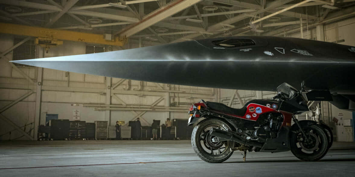 黑色摩托車停放在機庫中的隱形戰鬥機下方。 — 捍衛戰士：獨行俠 壁紙