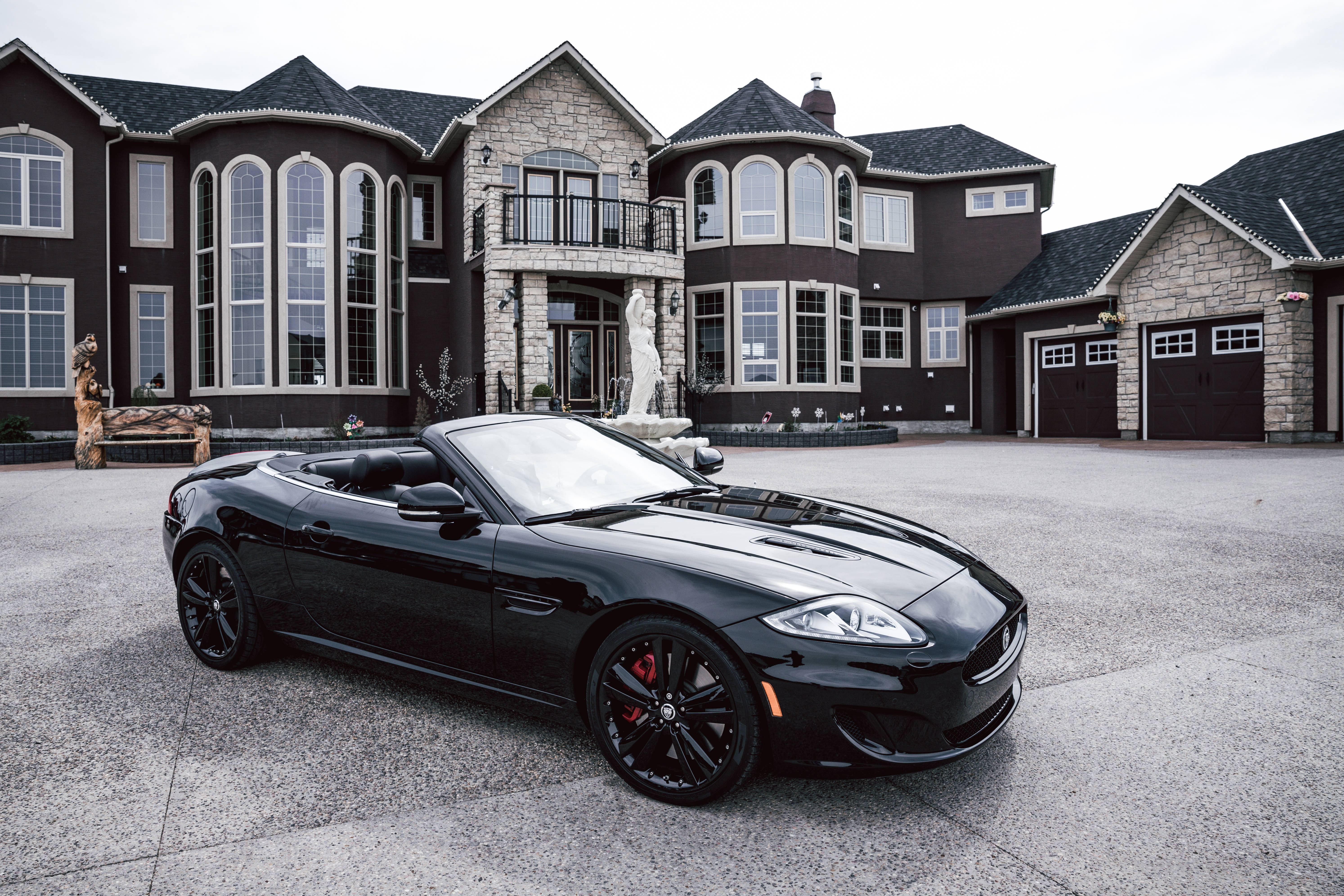 Maserati 桌布 壁紙 — 一架時尚的黑色敞篷跑車停在一棟帶有石頭裝飾和大窗戶的宏偉深棕色豪宅前。