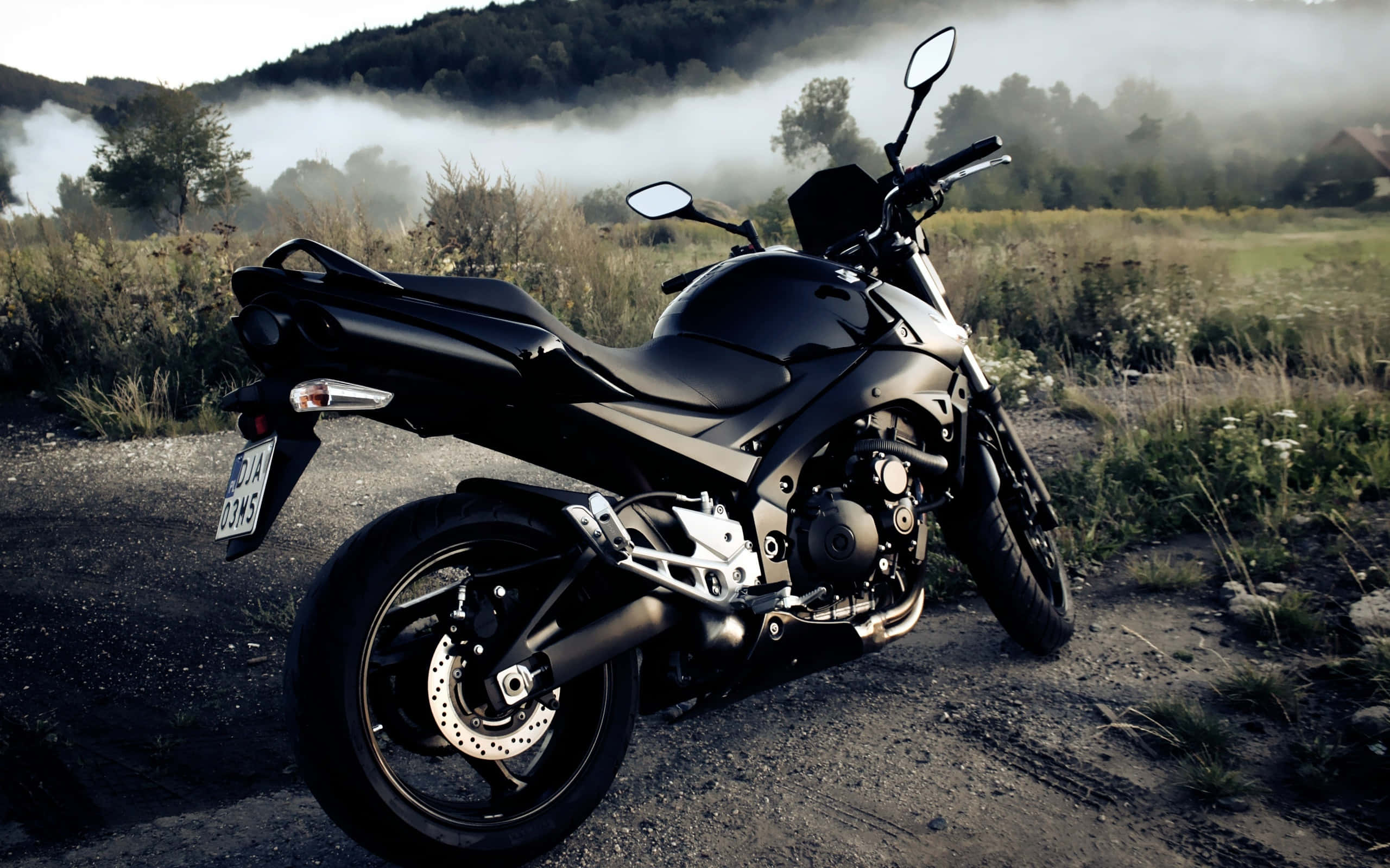 motorbike 桌布 壁紙 — 一架時尚的黑色機車停泊在碎石路上，黎明時分薄霧籠罩著樹木茂密的山坡。