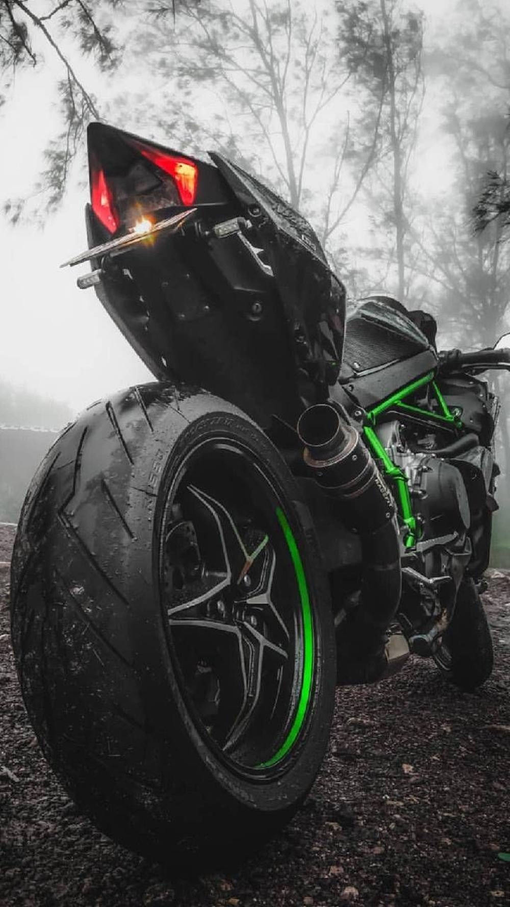 機車 桌布 壁紙 — 一架時尚的黑色機車帶有發光的綠色點綴，停在霧氣瀰漫的森林小徑上，尾燈在灰色的晨霧中閃爍著紅光。