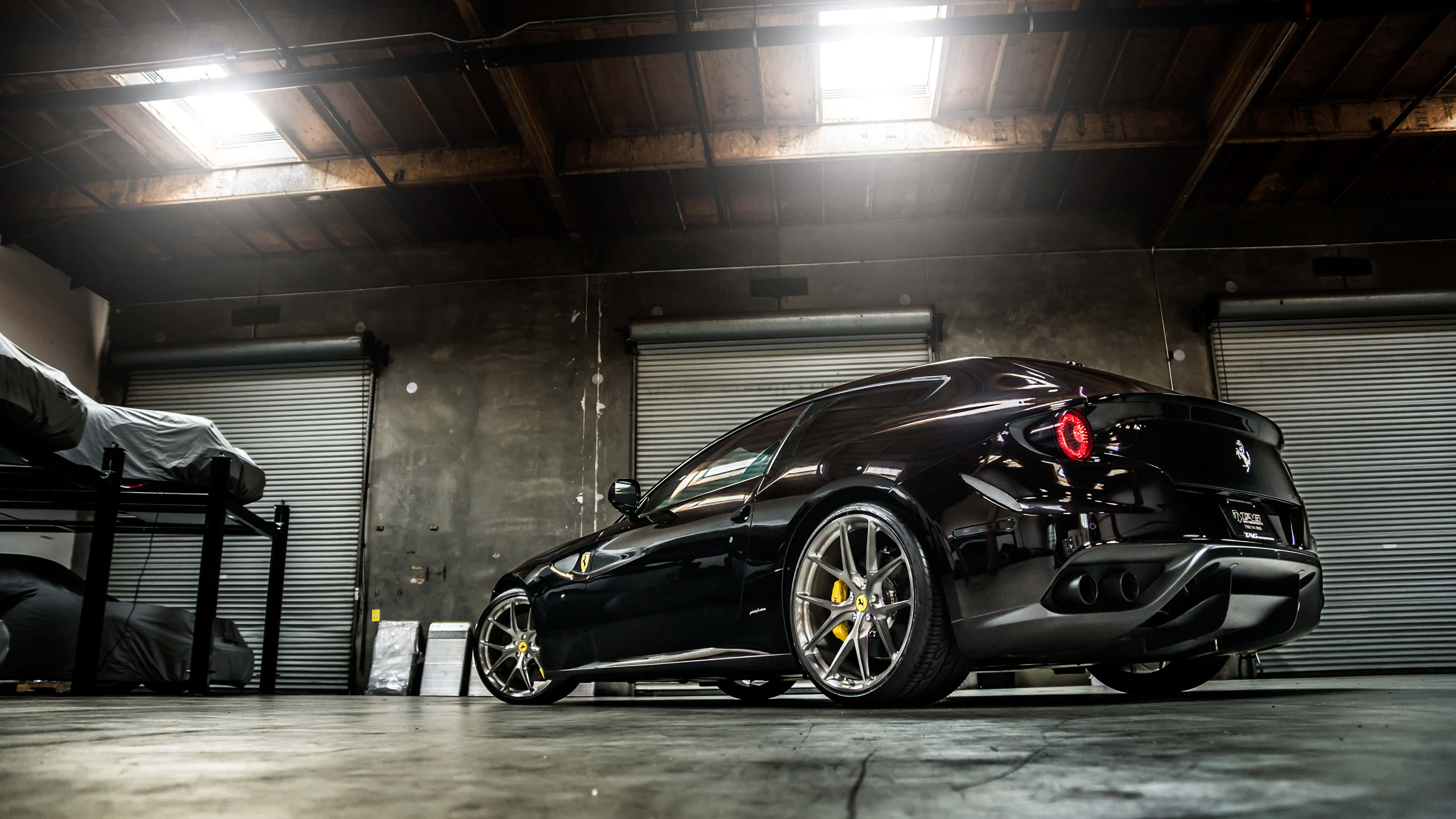 Ferrari Ff 桌布 壁紙 — 一架時尚的黑色法拉利跑車在工業燈光下，於粗糙的混凝土車庫中閃閃發光。