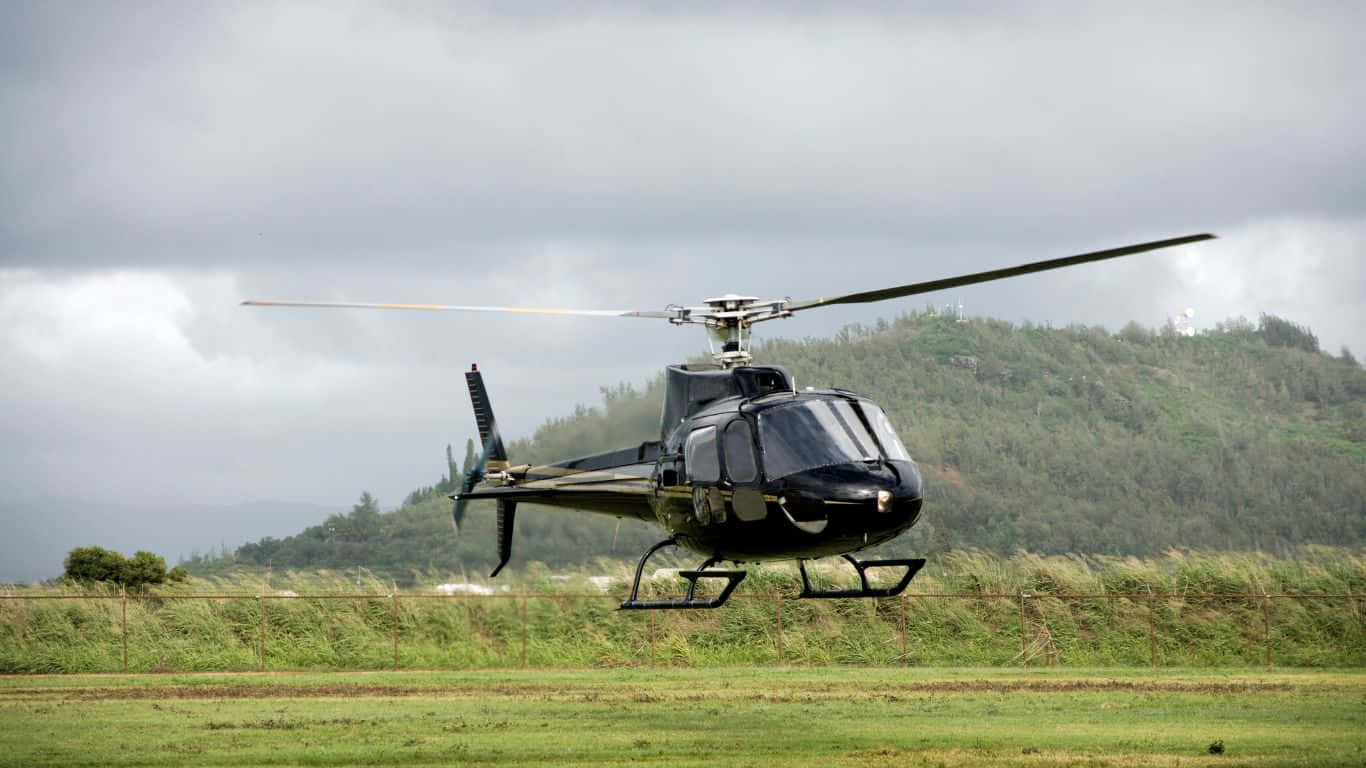 1366x768 Helicopters 桌布 壁紙 — 一架時尚的黑色直升機低空盤旋在草地上，附近有樹木繁茂的山丘，天空多雲。