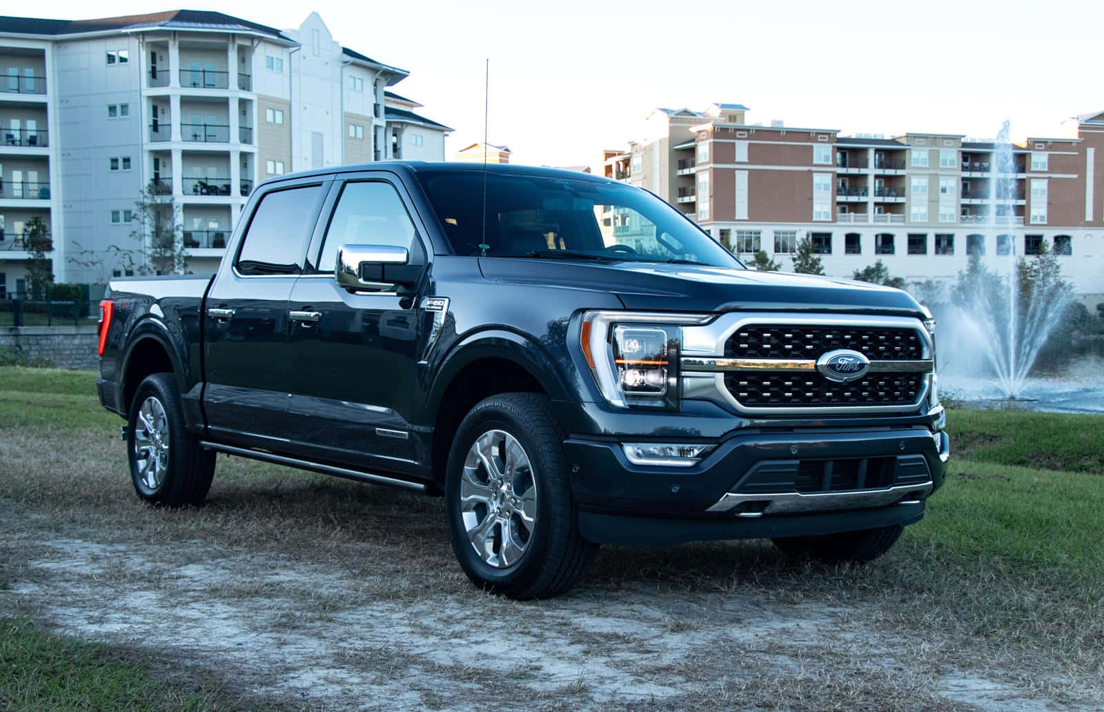 Ford Truck 桌布 壁紙 — 一架時尚的黑色福特F-150皮卡車停在噴泉附近的草地上，背景是公寓大樓。