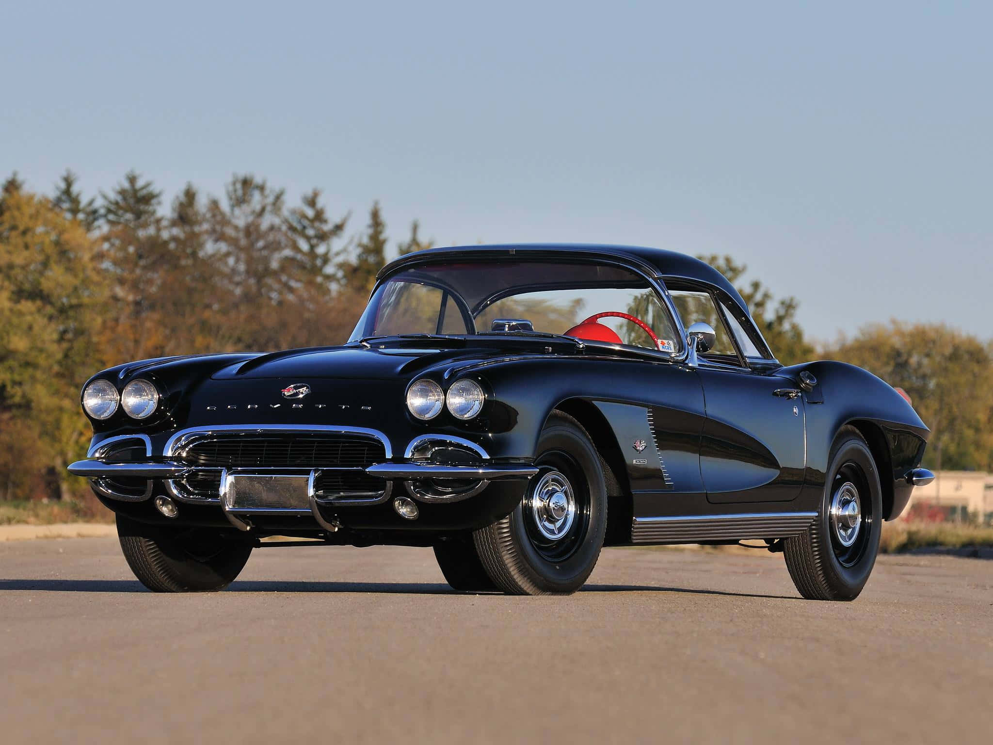 classic 桌布 壁紙 — 一架時尚的黑色經典Corvette跑車，帶有鍍鉻裝飾和紅色內飾，停在柏油路上，背景是秋天的樹木。