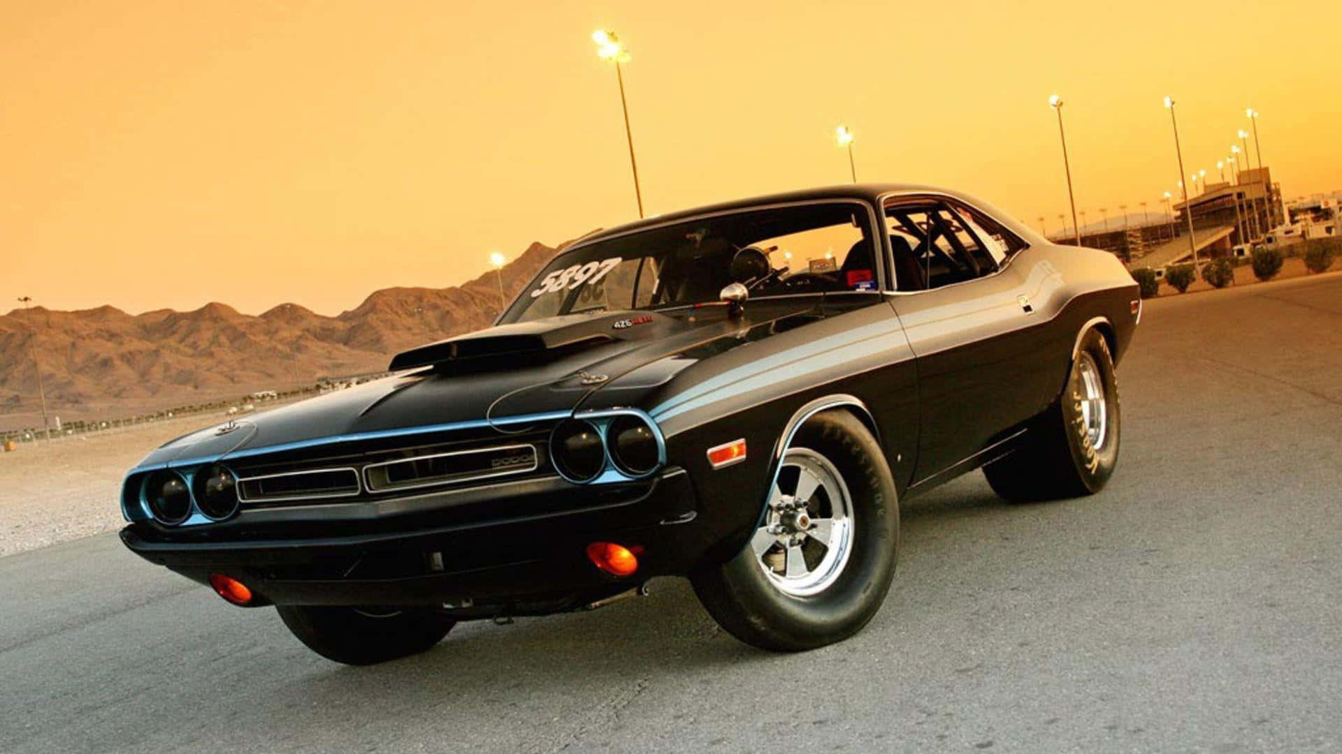 Fast And Furious 1 桌布 壁紙 — 一架時尚的黑色經典肌肉車，帶有藍色飾邊，停泊在賽道上，正值黃金時刻，背景是沙漠山脈。