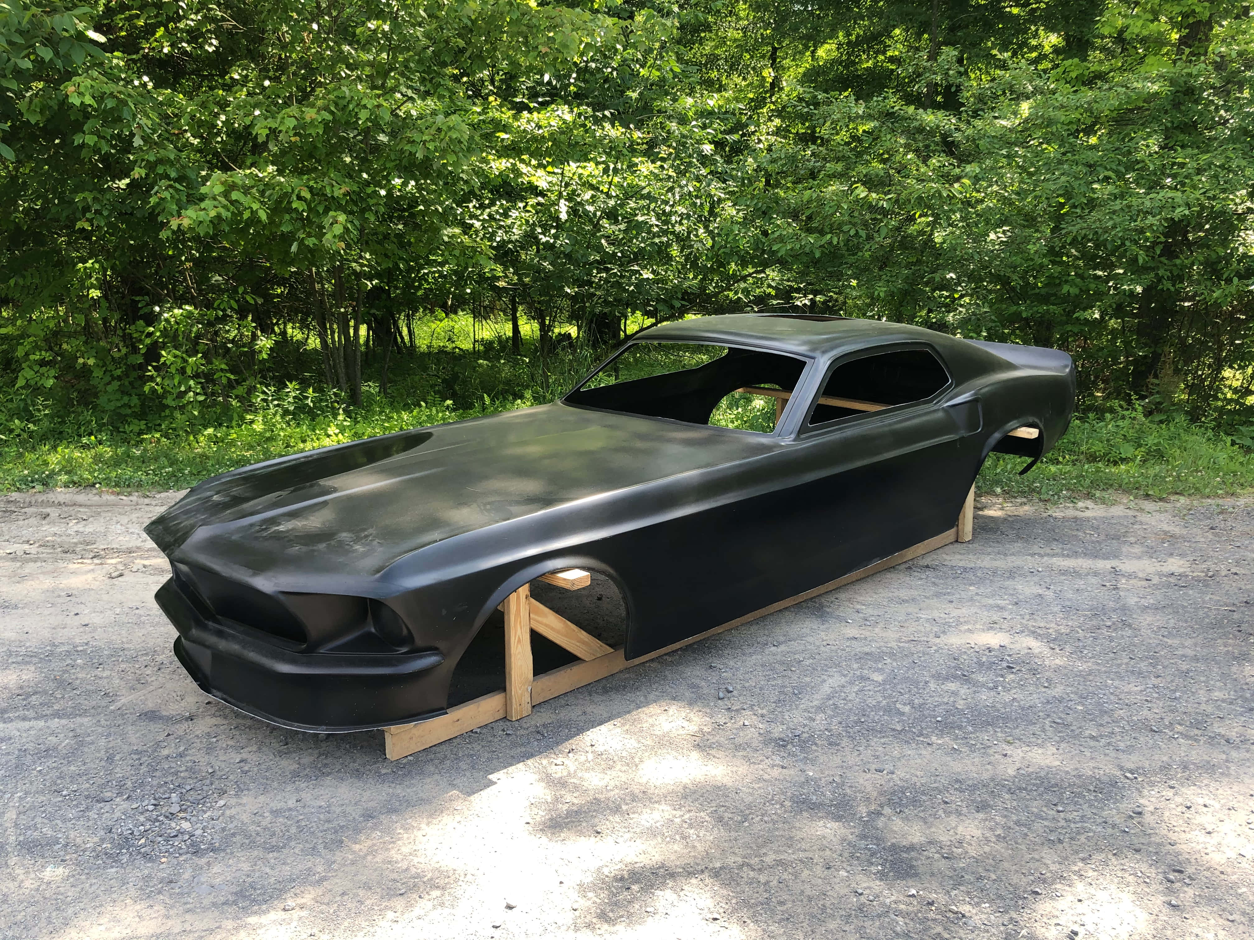 cars 桌布 壁紙 — 一架時尚的黑色經典肌肉車車身放置在陽光普照的森林空地的木製支架上。