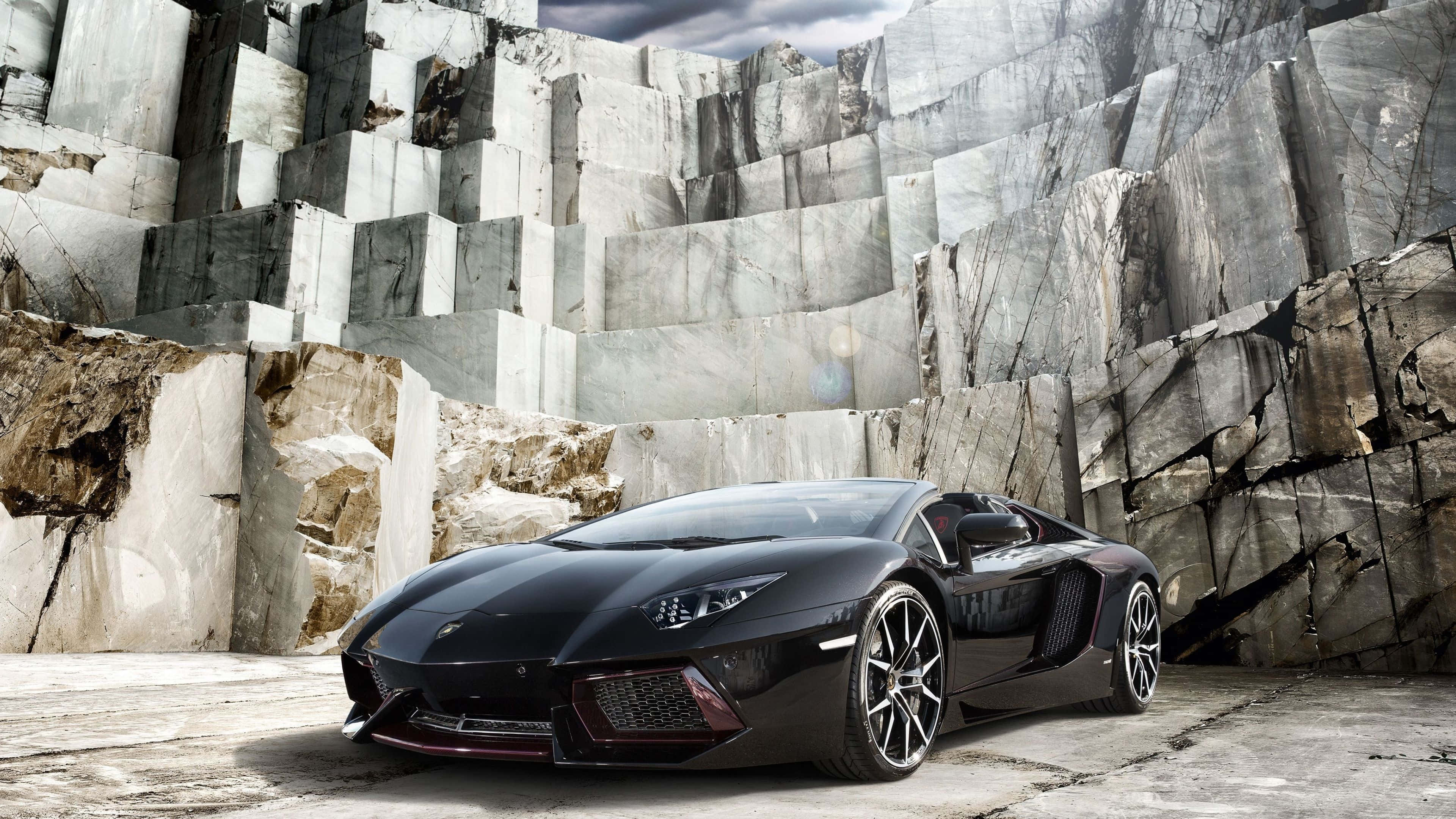 4K 藍寶堅尼 桌布 壁紙 — 一架時尚的黑色藍寶堅尼 Aventador 停放在巨大大理石懸崖前，天空多雲。