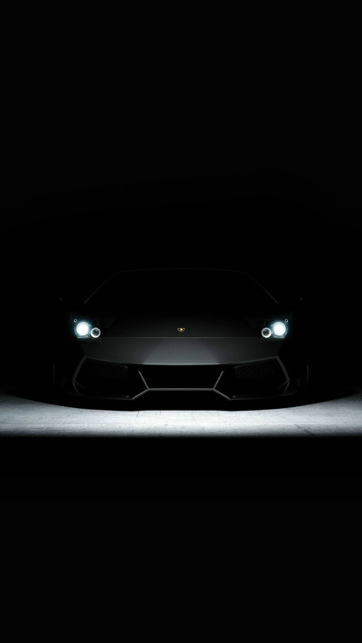 elegant 桌布 壁紙 — 一架時尚的黑色藍寶堅尼跑車從黑暗中出現，發光的車頭燈照亮了混凝土地板。