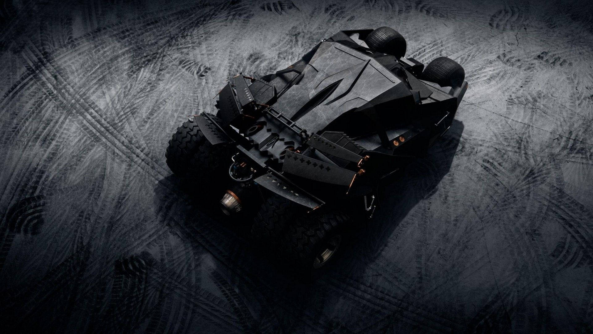 Batmobile 桌布 壁紙 — 一架時尚的黑色裝甲車停在粗糙的地面上，地面有輪胎痕跡，在戲劇性的燈光下。