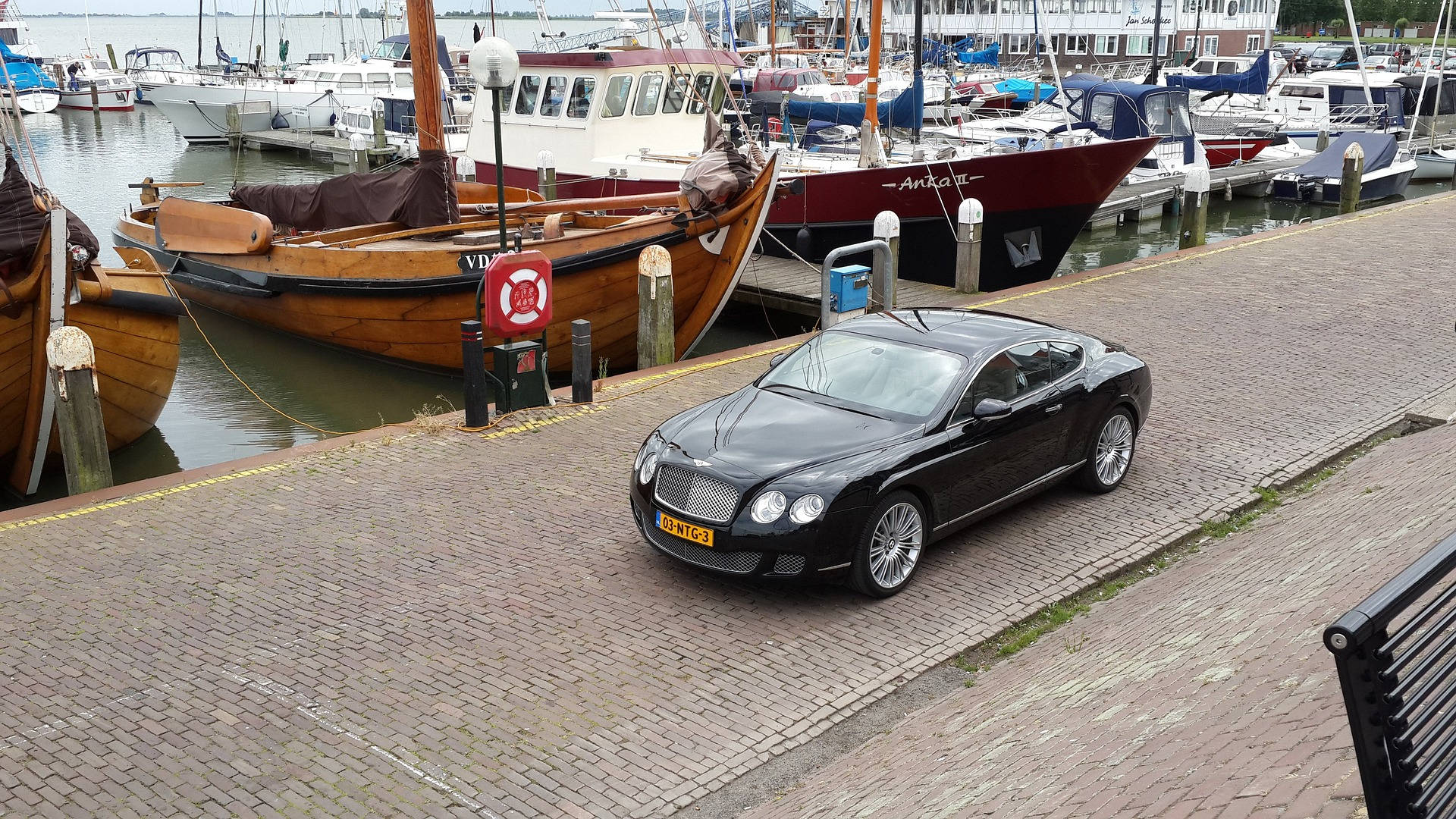Port 桌布 壁紙 — 一架時尚的黑色賓利 Continental GT 停泊在繁忙港口的磚砌碼頭上，旁邊是經典的木船。