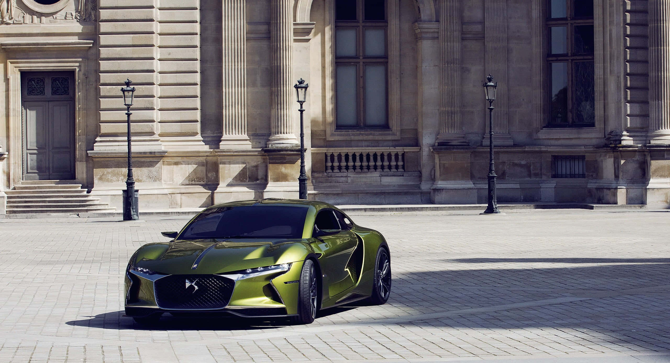 Ds Automobiles 桌布 壁紙 — 一架時尚金屬綠色跑車停泊在陽光普照的鵝卵石廣場上，前方是一座宏偉的古典石建築。
