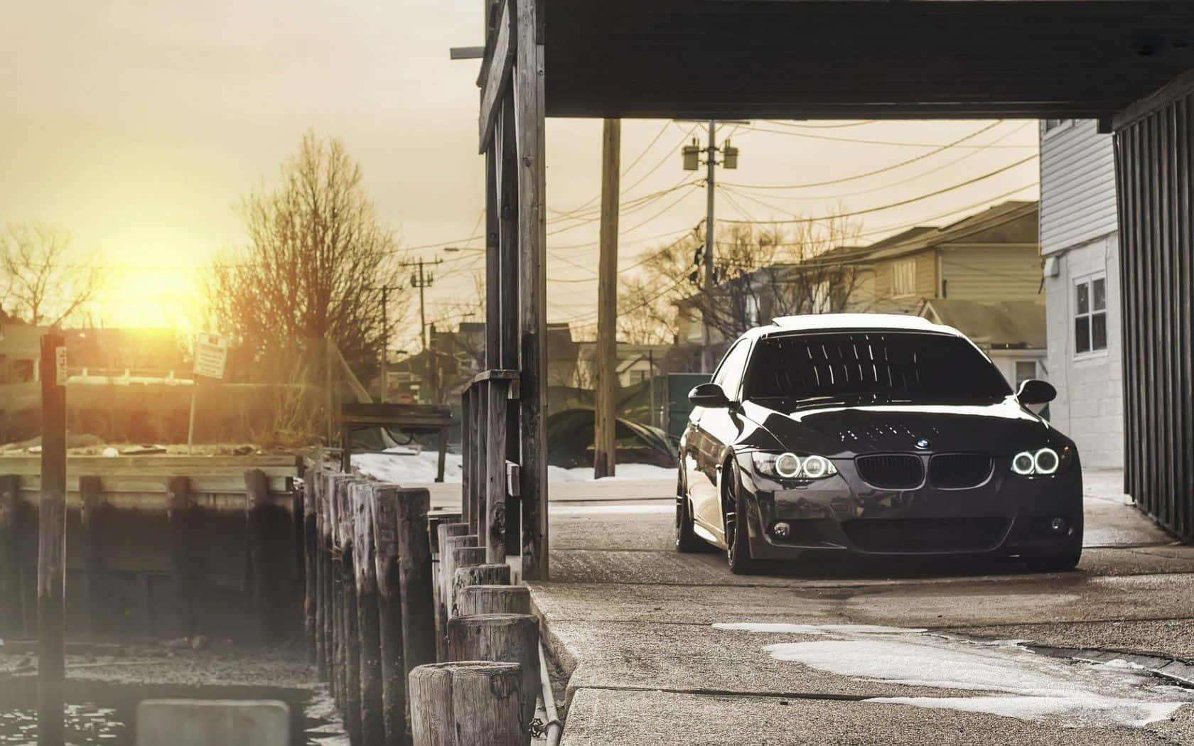 Bmw 328 桌布 壁紙 — 一架時尚黑色BMW跑車停放在木結構下，金色夕陽灑滿積雪的都市海濱。