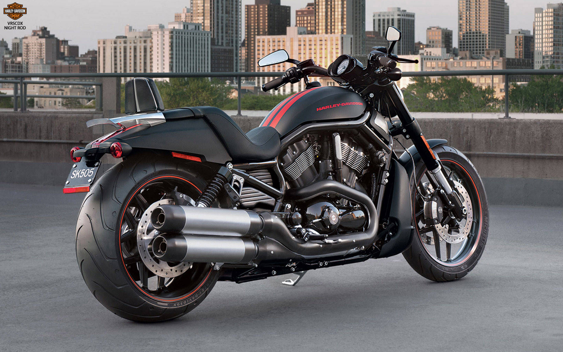 Cool Bike 桌布 壁紙 — 一架時尚黑色Harley-Davidson Night Rod機車，帶有紅色點綴，停放在城市屋頂，俯瞰現代天際線，時值黃昏。