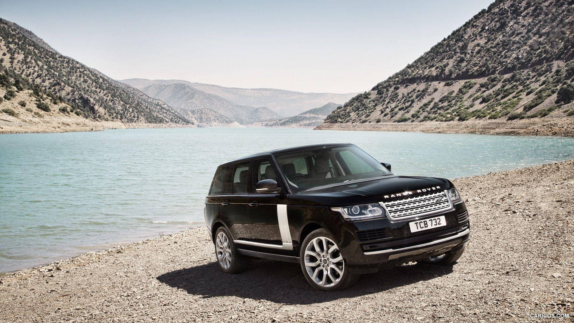  壁紙 — 一架時尚黑色Range Rover SUV停泊在岩石湖岸上，背後乾旱山脈在晴朗天空下聳立。