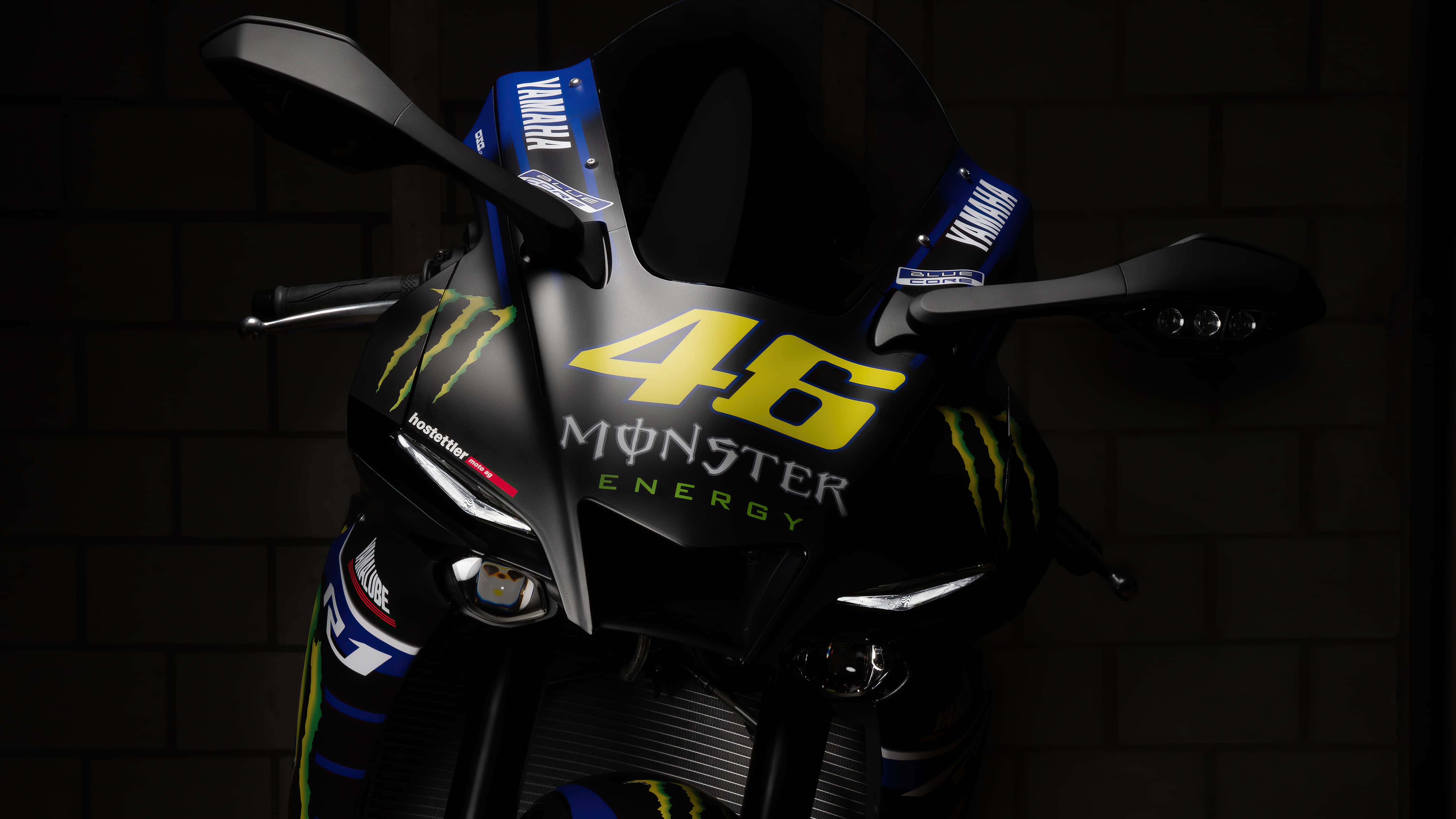 攝影 桌布 壁紙 — 一架時尚黑色Yamaha機車，帶有醒目的黃色46 Monster Energy品牌標誌，在深色磚牆前被戲劇性地照亮。