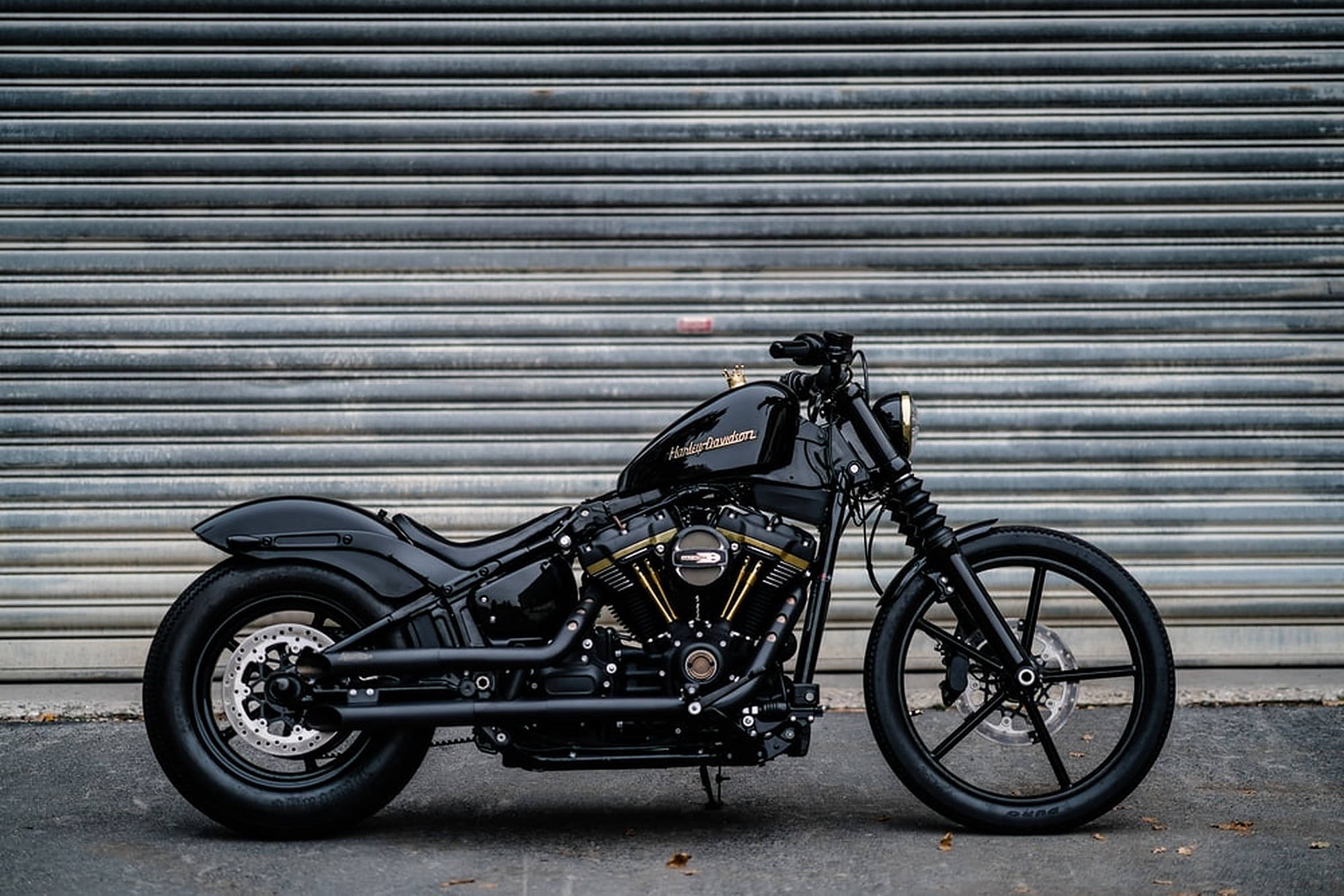 Chopper 桌布 壁紙 — 一架時尚黑色哈雷機車配金色點綴，停靠在波紋金屬車庫門前。