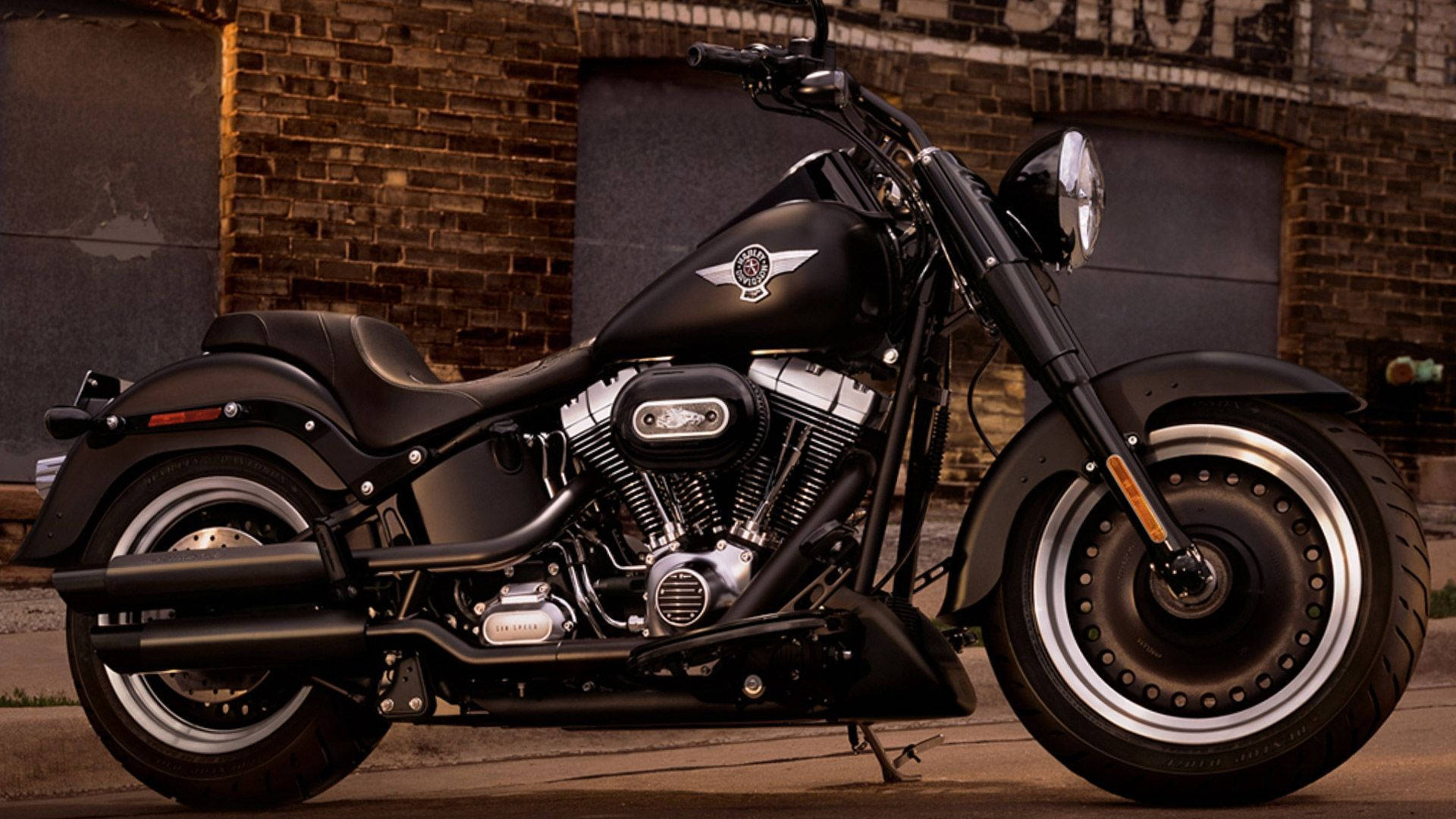 Harley 桌布 壁紙 — 一架時尚黑色巡航機車配以鍍鉻裝飾，停靠在風化磚牆旁，沐浴在溫暖金色光線下。